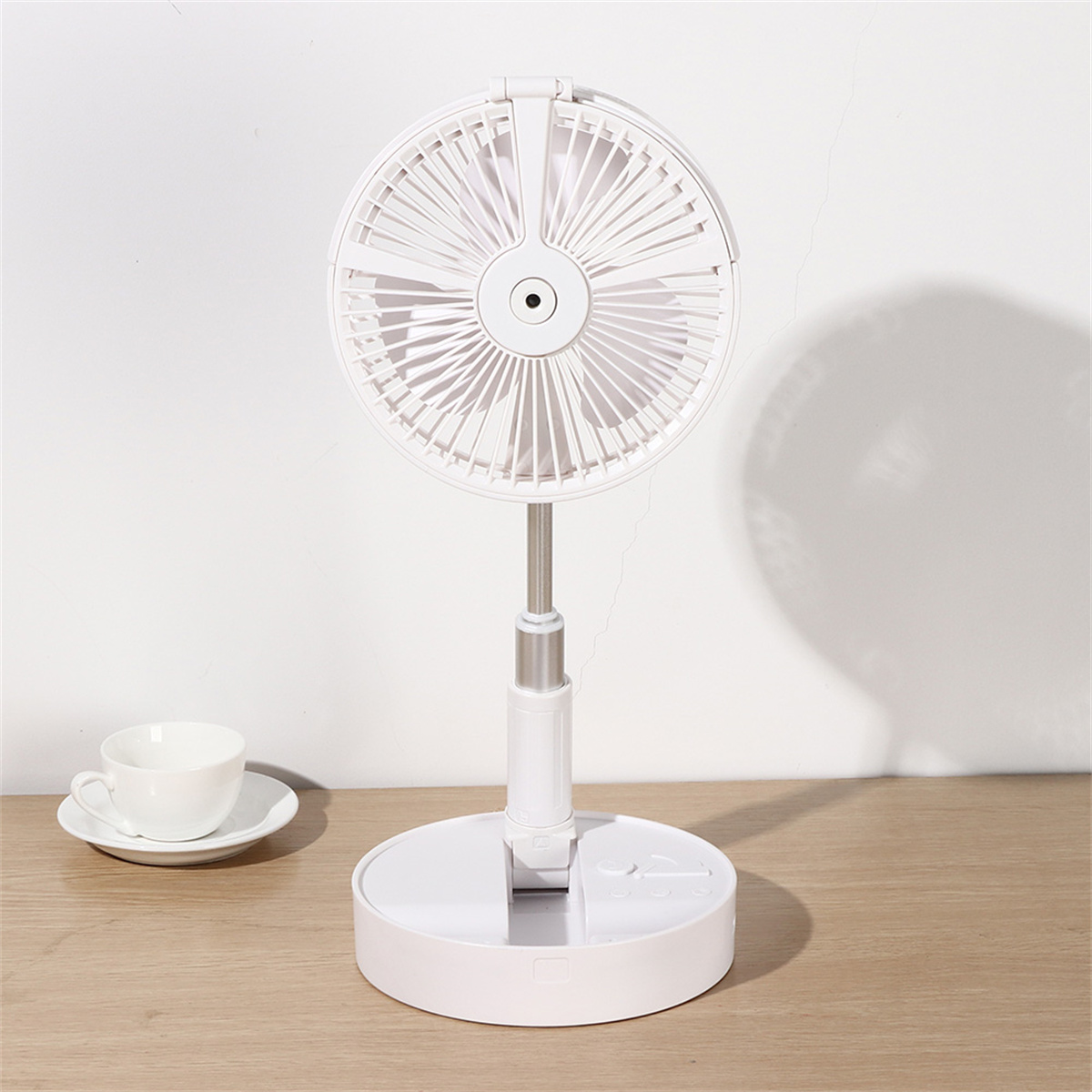 Weißer tragbarer Ventilator, runder Sockel, höhenverstellbar, auf einem Holztisch, mit Tasse und Untertasse.