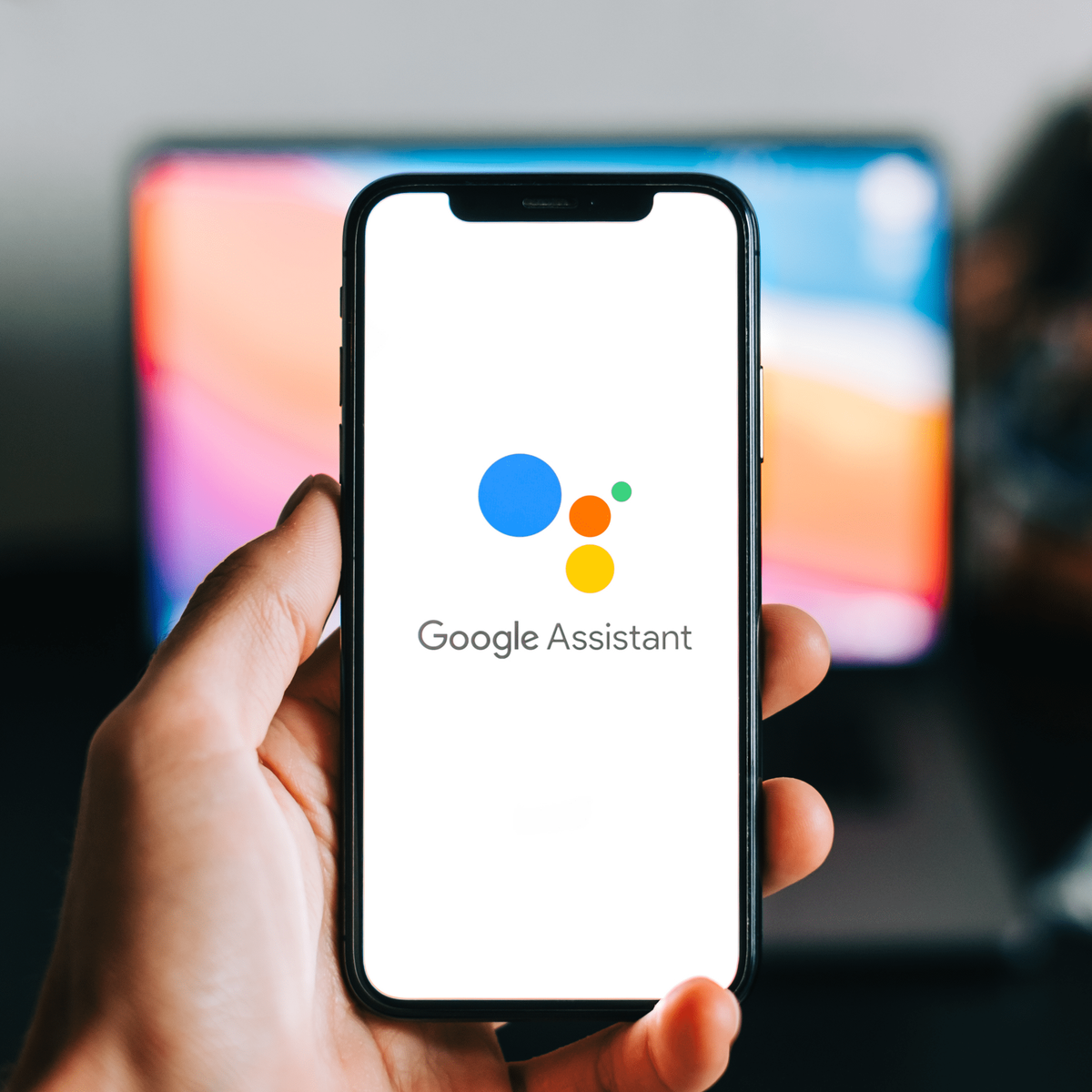 Una mano sosteniendo un smartphone con el logo de Google Assistant.