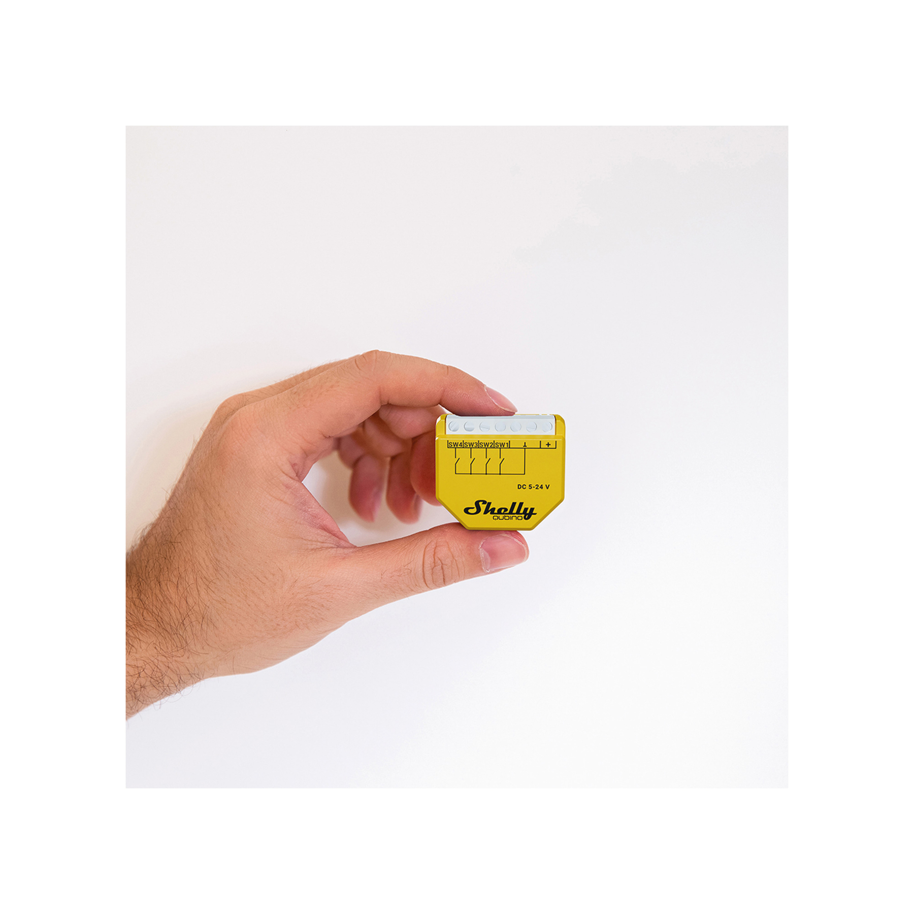 Une main tenant un appareil électronique jaune, de forme carrée, avec des ports et du texte.