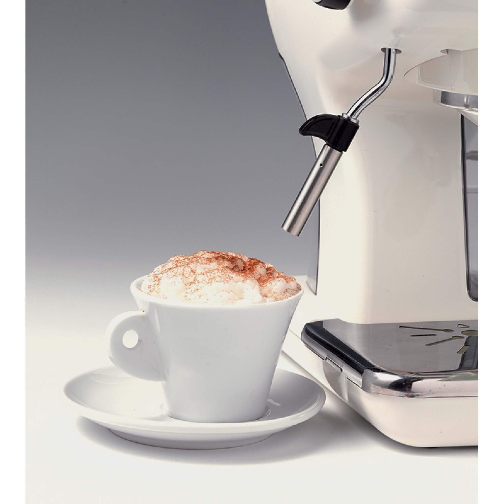 Filiżanka cappuccino z białą filiżanką i spodkiem ceramicznym, obok białego ekspresu do kawy.