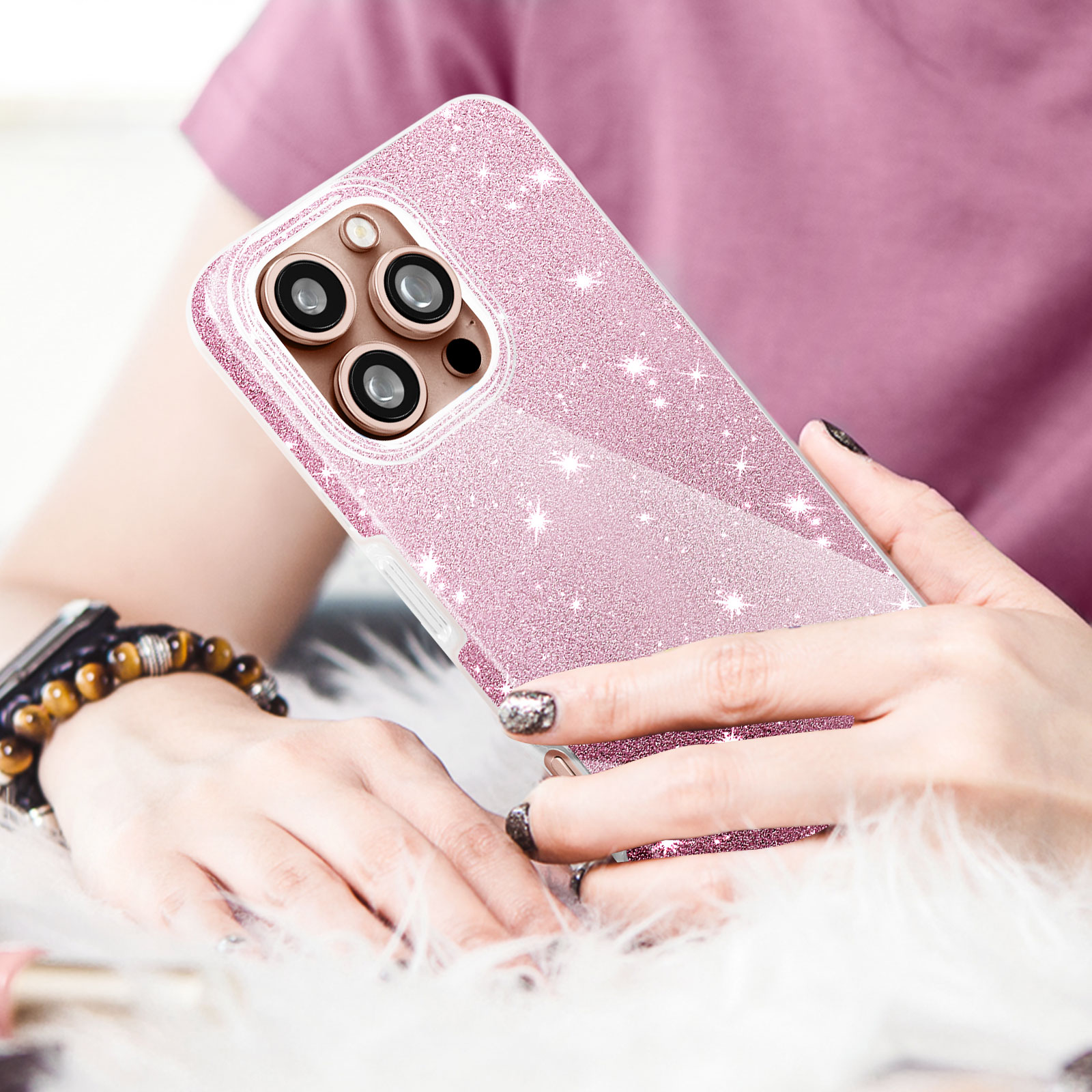Una persona tiene in mano una custodia rosa glitterata con una fotocamera. Sono visibili un braccialetto e della pelliccia.