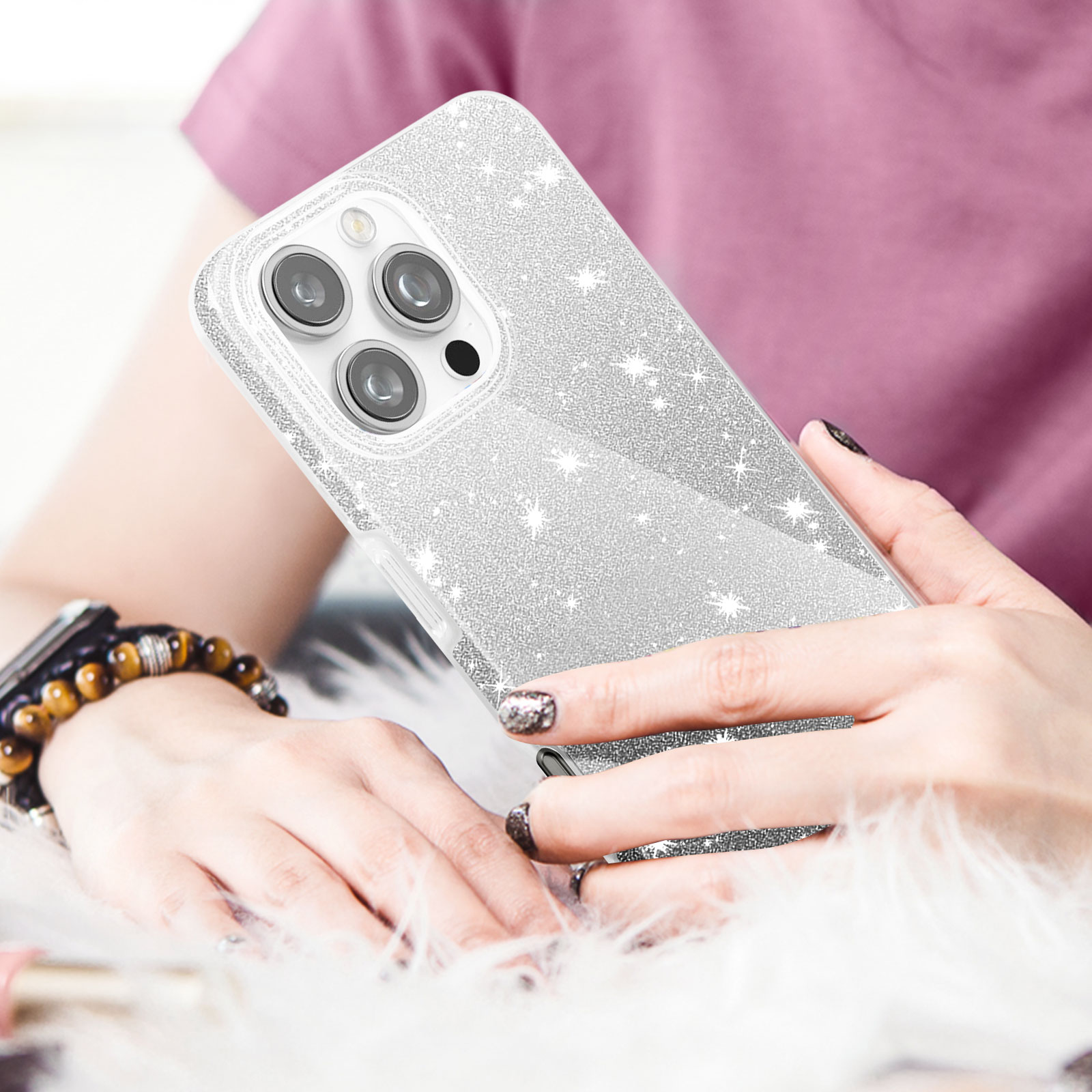 Una persona tiene in mano un telefono con una custodia glitterata. La custodia riflette la luce. Visibili bracciale e unghie.