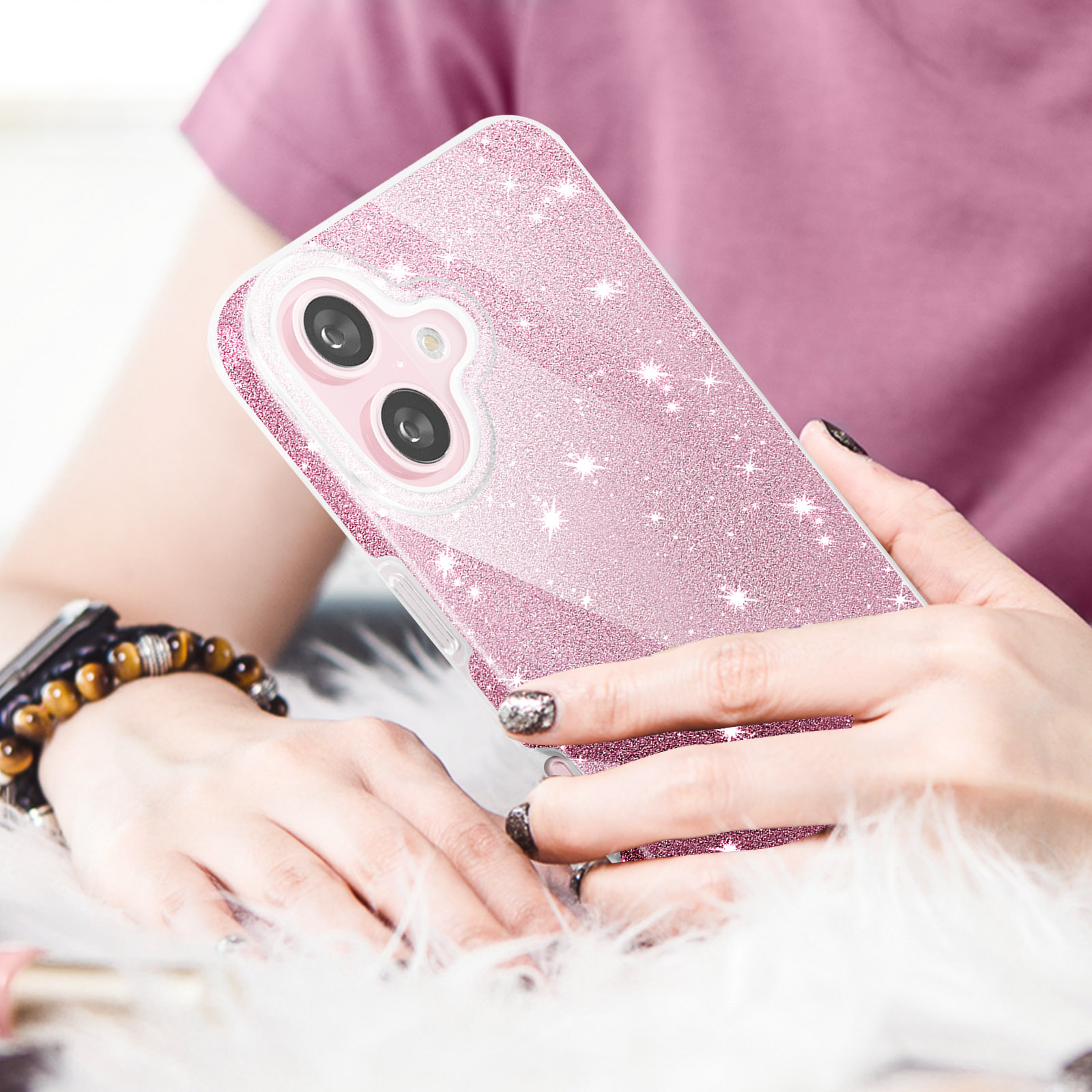 Una persona tiene in mano una custodia rosa glitterata. Lo sfondo include una camicia rosa e pelliccia bianca.