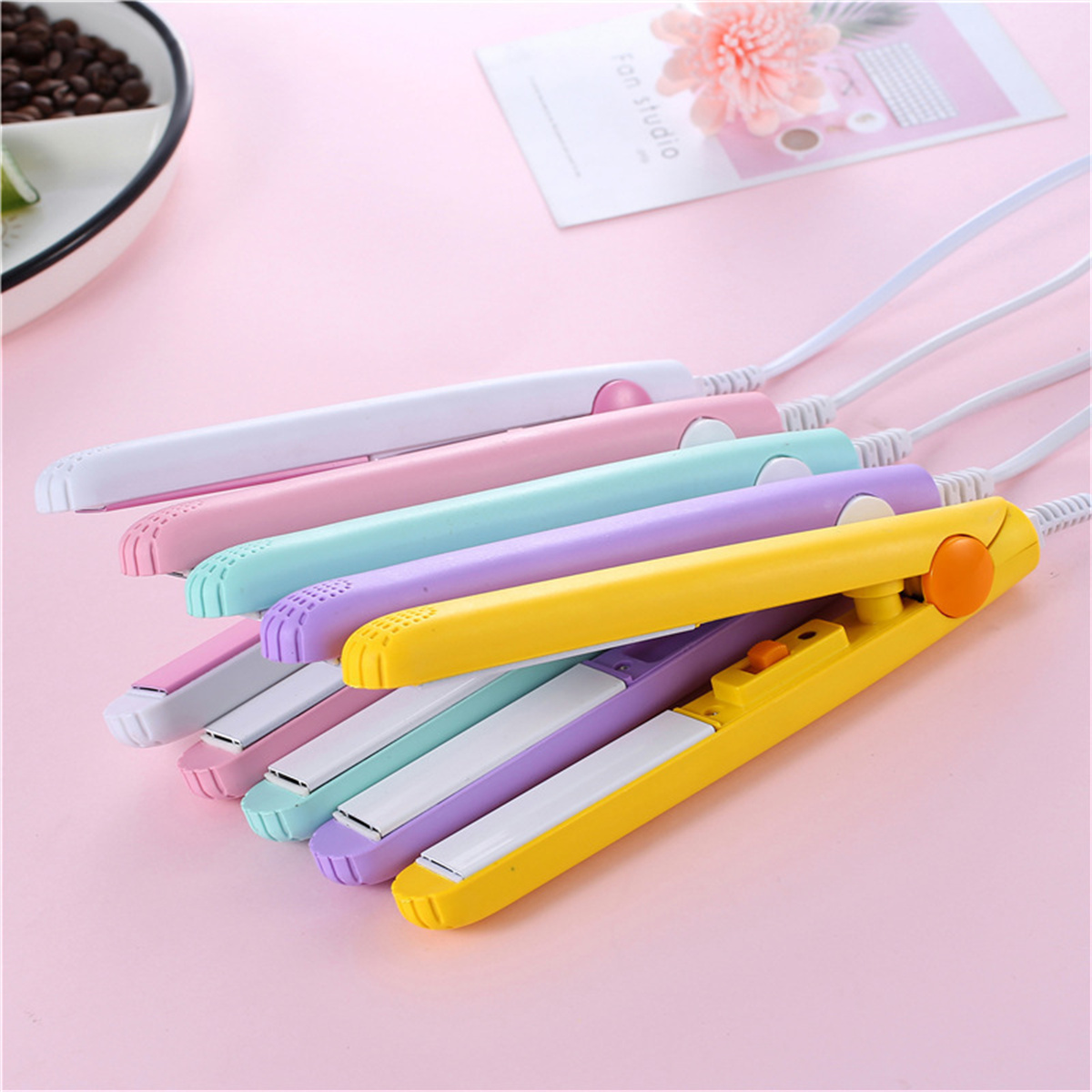 Mehrere bunte Haarglätter sind ausgelegt. Sie sind in Gelb, Rosa, Lila, Grün und Weiß gehalten.