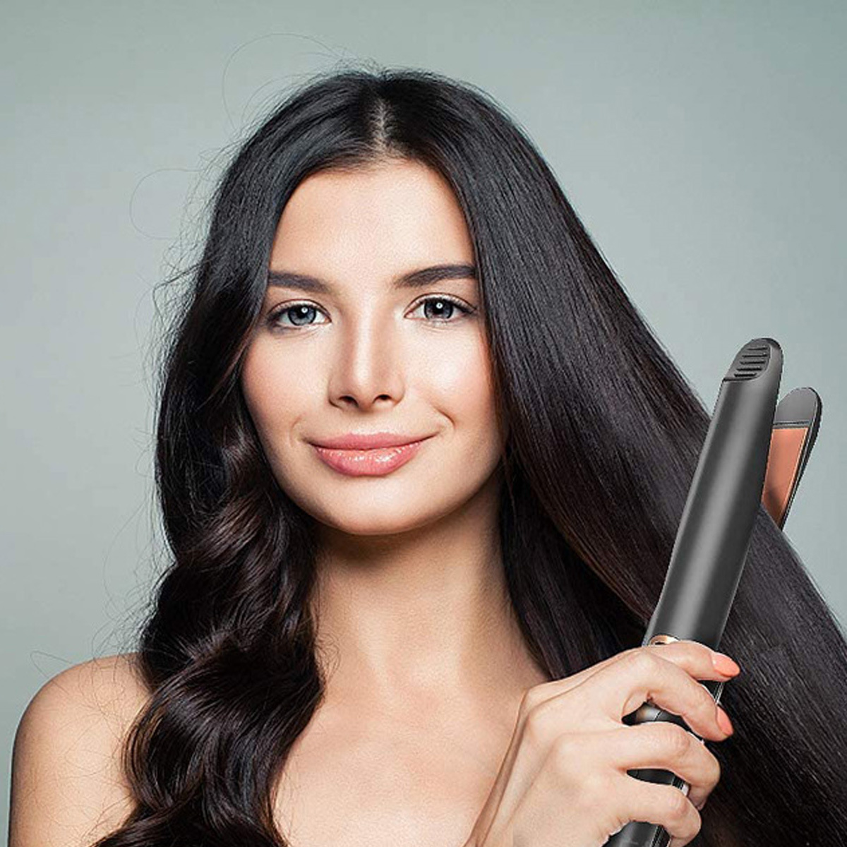 Frau mit langen schwarzen Haaren, die einen schwarzen Haarglätter benutzt, lächelt.