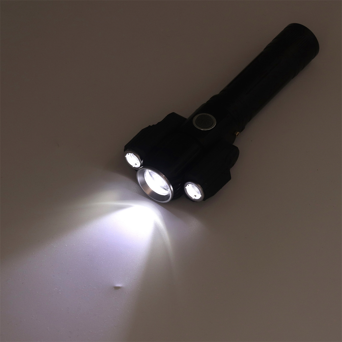 Eine schwarze Taschenlampe mit drei kleineren Lichtern. Lichtstrahl scheint auf graue Oberfläche.