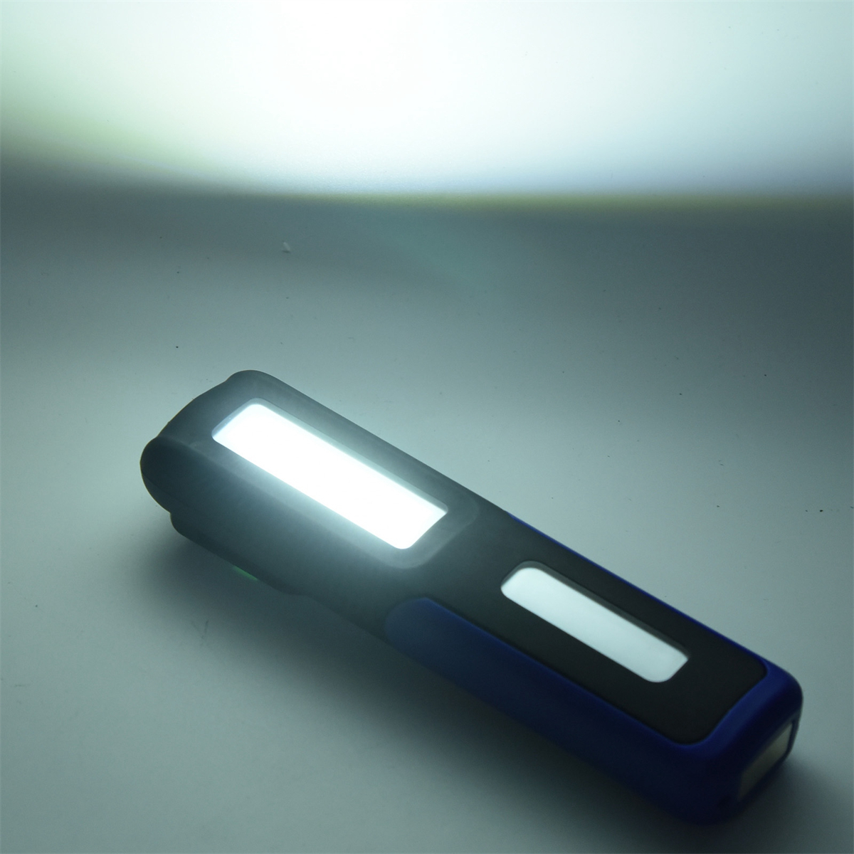 Blau-schwarze Taschenlampe, die ein starkes weißes Licht aussendet, auf einer weißen Oberfläche.