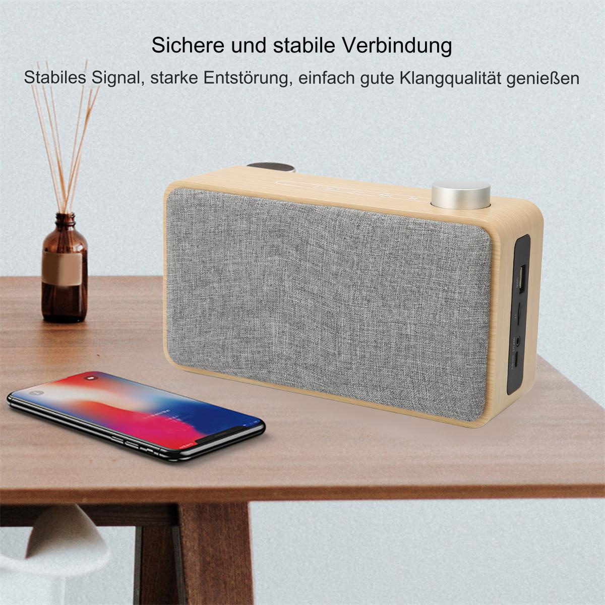 Ein hölzerner Lautsprecher auf einem Tisch mit einem Telefon, das ein Ladesymbol zeigt, und einer Flasche.