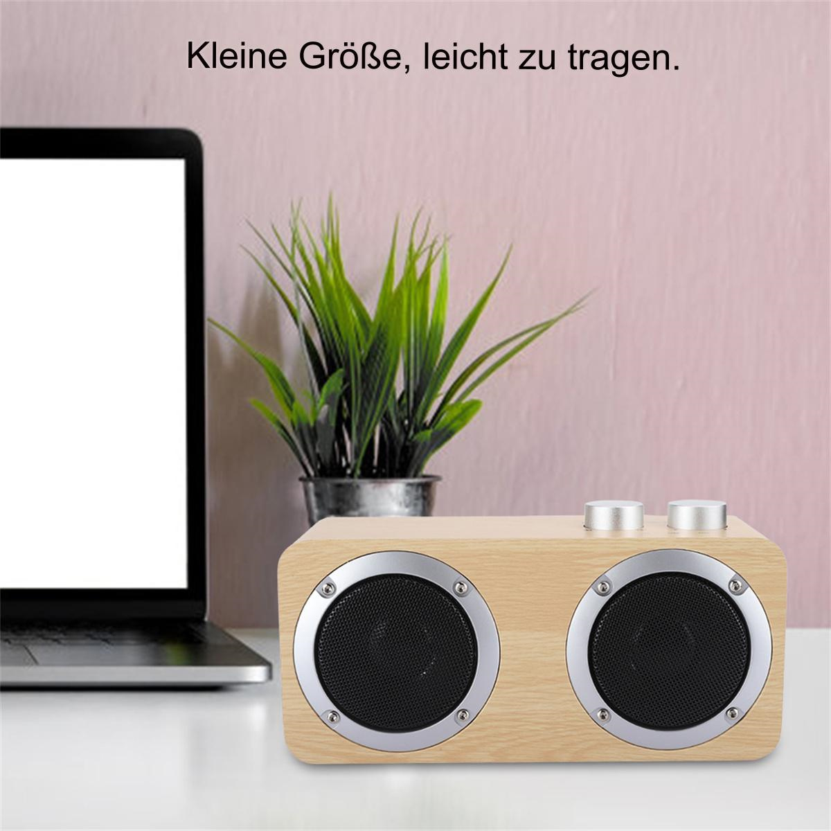 Holzlautsprecher mit zwei Lautsprechern und silbernen Bedienelementen auf einem weißen Tisch, mit einer Pflanze.