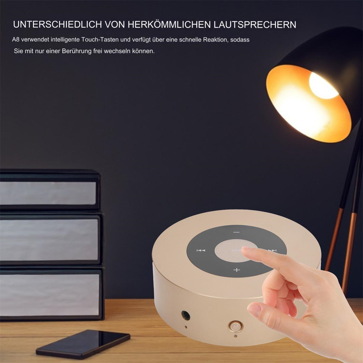 Eine Hand berührt einen goldfarbenen, runden Lautsprecher mit Touch-Bedienelementen, ein schwarzes Telefon und eine Lampe.