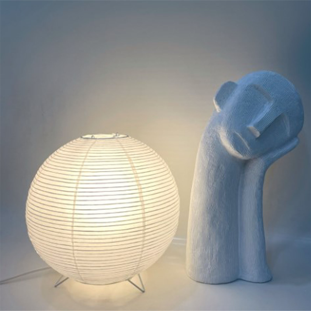 Eine weiße Papierlaterne mit Licht und eine weiße Skulptur einer Person mit gesenktem Kopf.