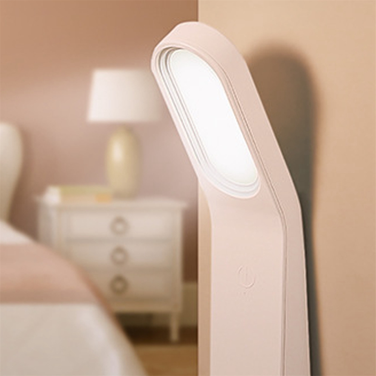 Rosa Lampe an einer Wand. Die Lampe hat ein weißes Licht. Der Hintergrund ist ein Schlafzimmer.