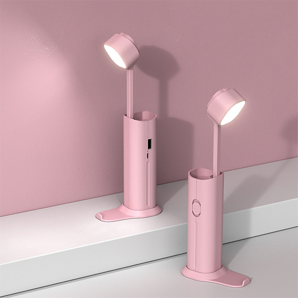 Zwei rosa Schreibtischlampen auf einer weißen Oberfläche. Beide sind an.