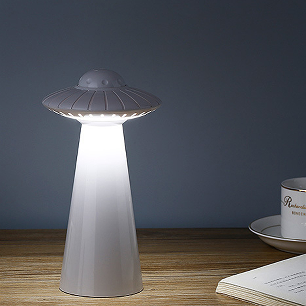 UFO-förmige Lampe auf Holzoberfläche mit Tasse und Buch in der Nähe.