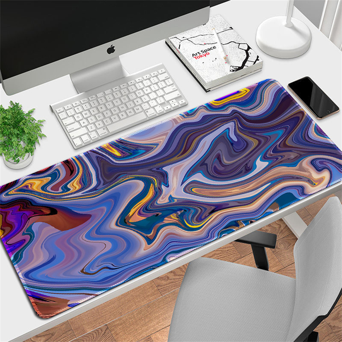 Ein Schreibtisch mit farbenfrohem, wirbelndem Mousepad, Tastatur, Monitor, Telefon und Pflanze.