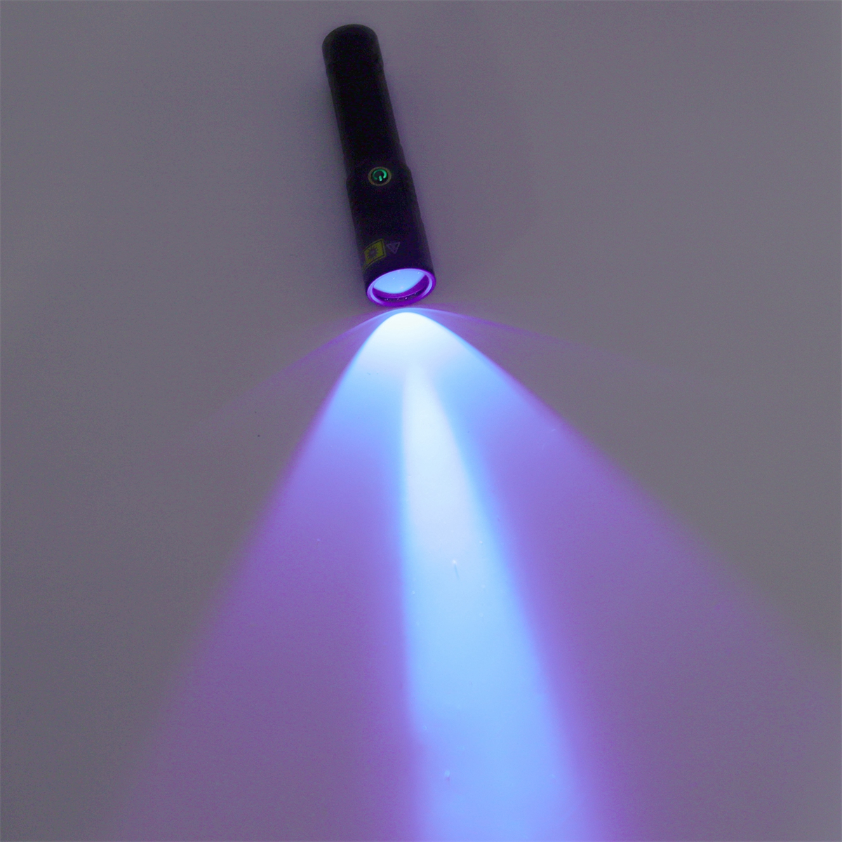 Eine schwarze Taschenlampe strahlt einen lila Lichtstrahl auf eine helle Oberfläche.