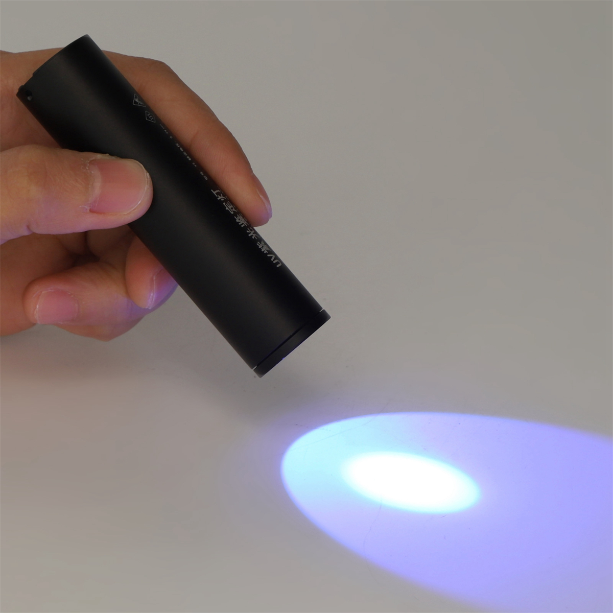Eine schwarze Taschenlampe, die blaues Licht auf eine weiße Oberfläche wirft, gehalten von einer Hand.