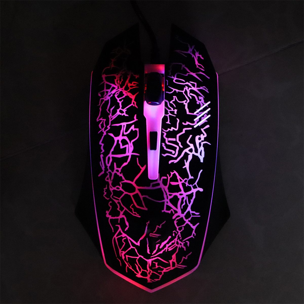 Eine schwarze Gaming-Maus mit farbenfrohen Rissen und leuchtenden Lichtern auf dunkler Oberfläche.