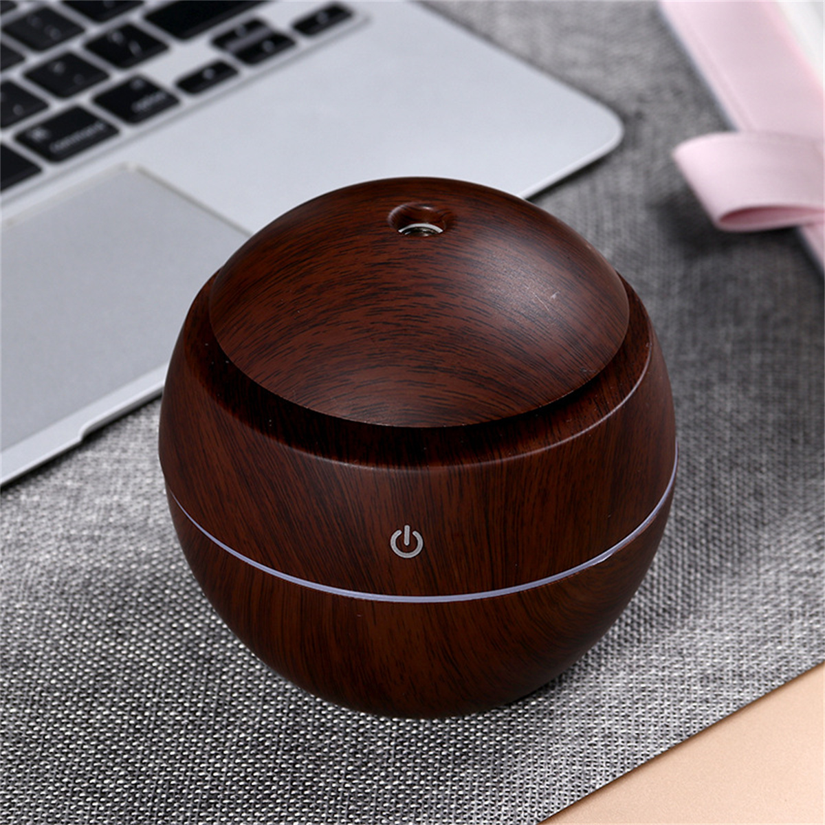 Ein brauner Aroma-Diffusor mit Holzmaserung. Der Hintergrund umfasst einen Laptop und eine rosa Box.
