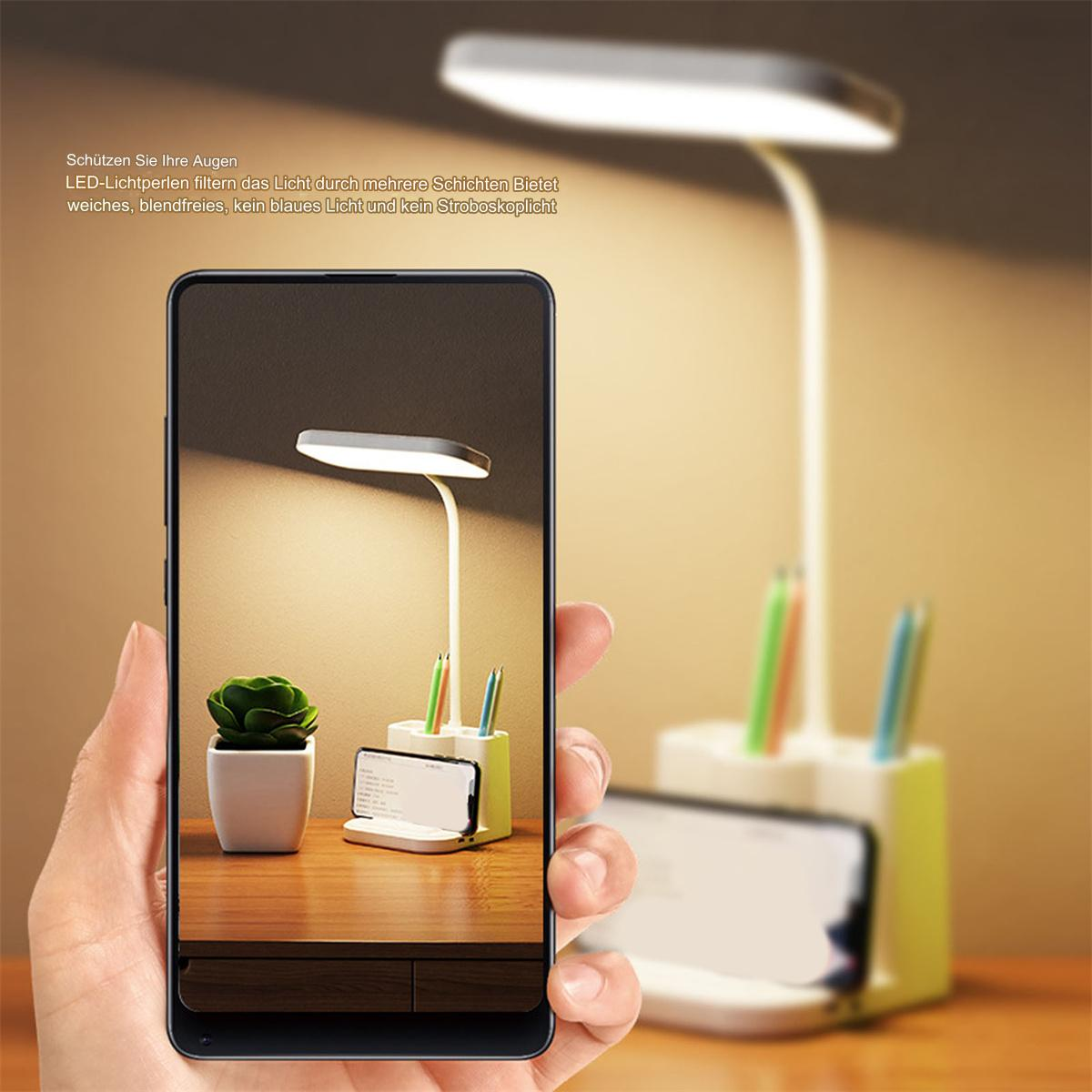 Eine Hand, die ein Telefon mit einer Schreibtischlampe und einer kleinen Pflanze zeigt.