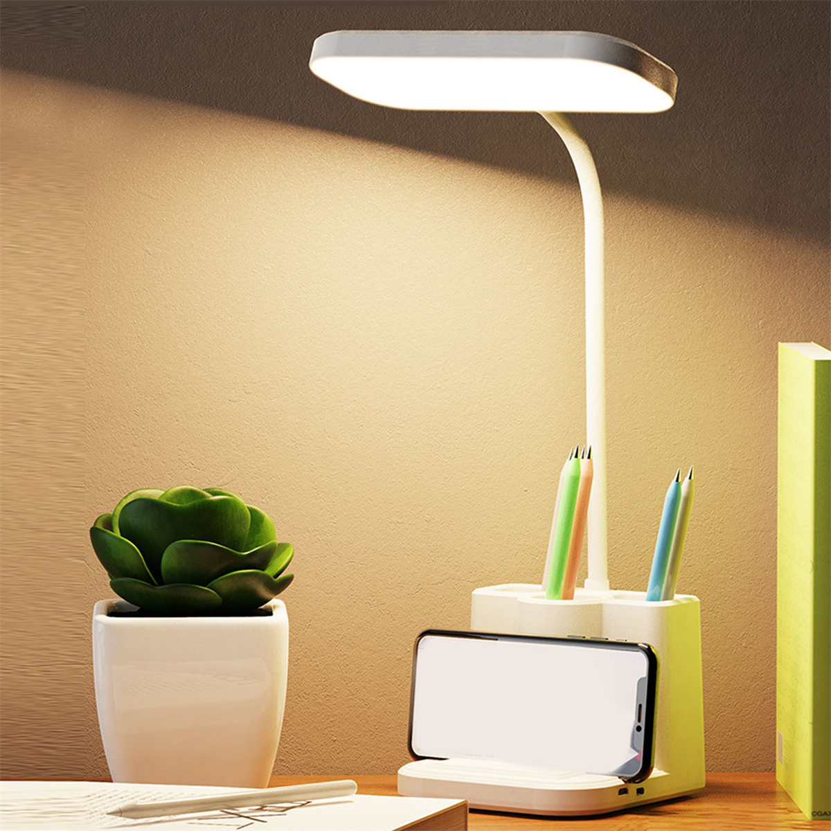 Eine Schreibtischlampe mit Pflanze, Stiften und Telefon. Die Lampe ist weiß mit Licht und Telefonhalter.
