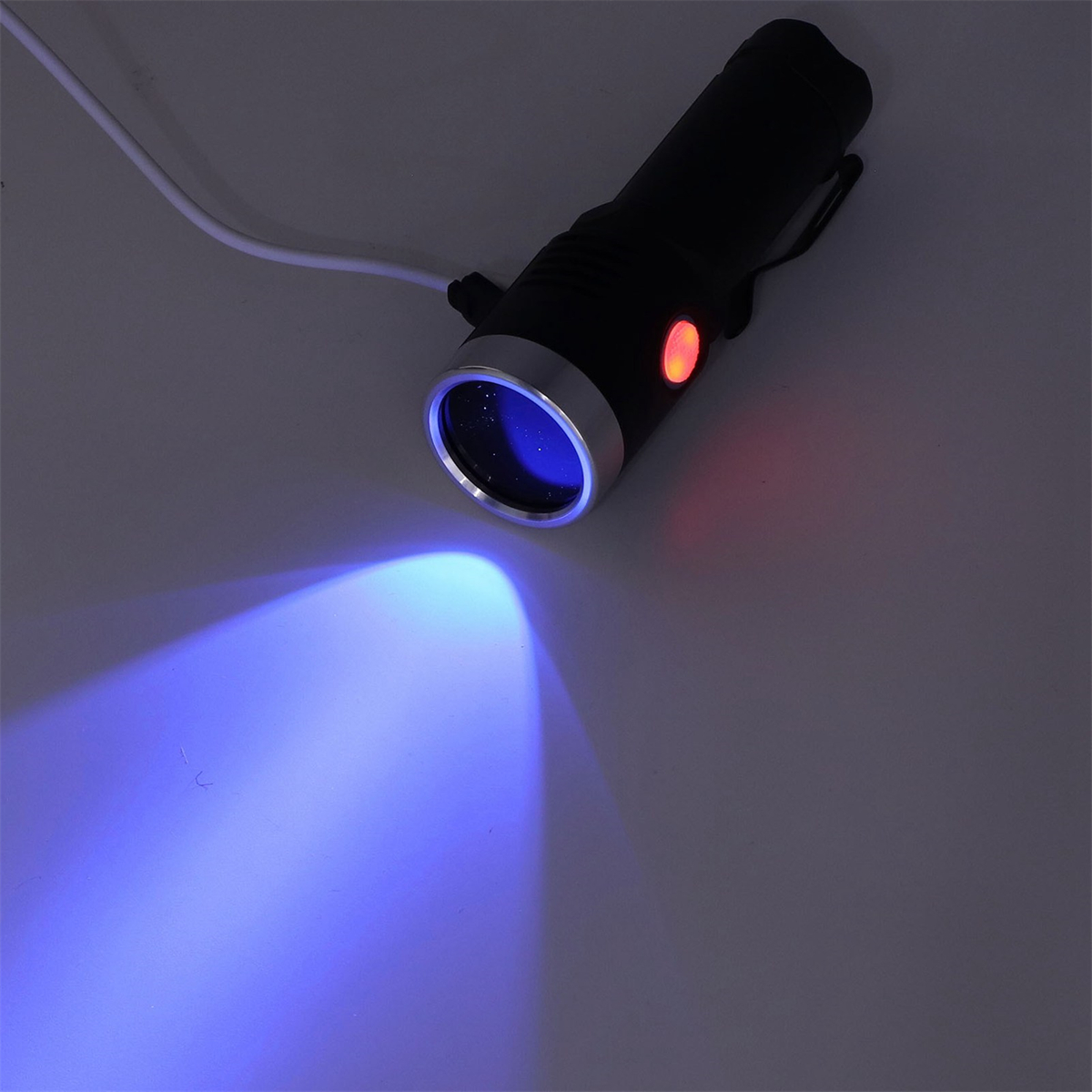 Eine schwarze Taschenlampe strahlt einen blauen Strahl aus. Die Taschenlampe hat ein rotes Licht an der Seite.