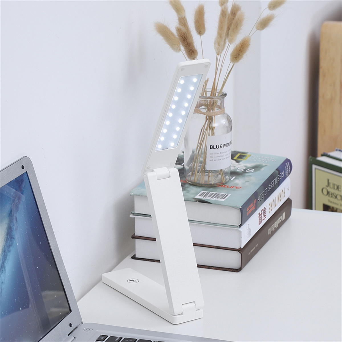 Weiße Schreibtischlampe mit verstellbarem Kopf, beleuchtet, auf einem Schreibtisch mit Büchern, Laptop.