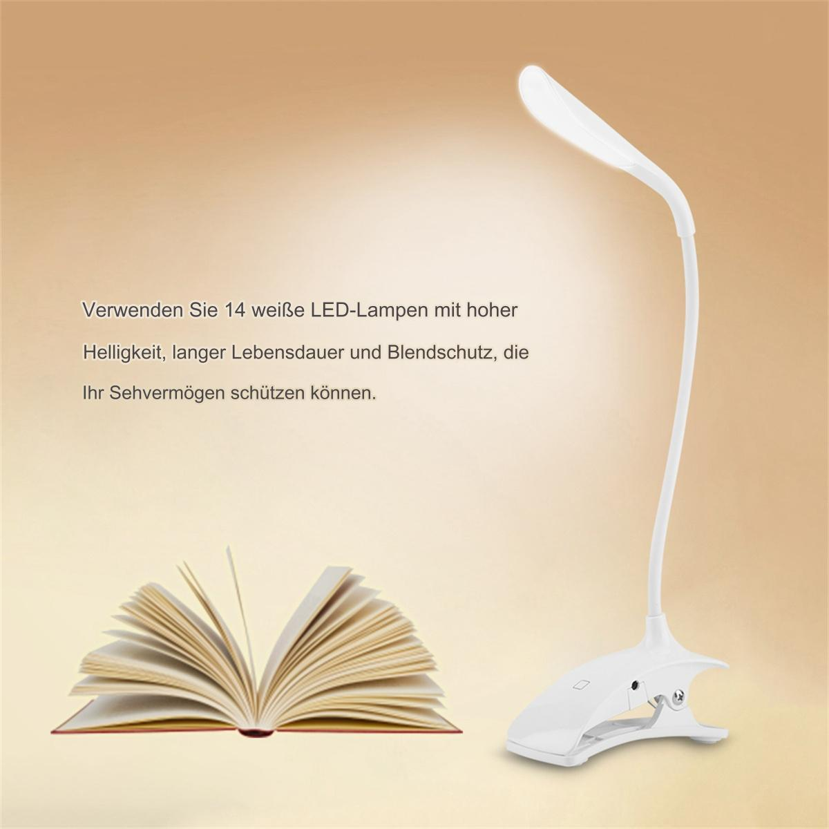 Eine weiße Schreibtischlampe mit Clipfuß. Ein offenes Buch befindet sich vor der Lampe auf einer braunen Oberfläche.