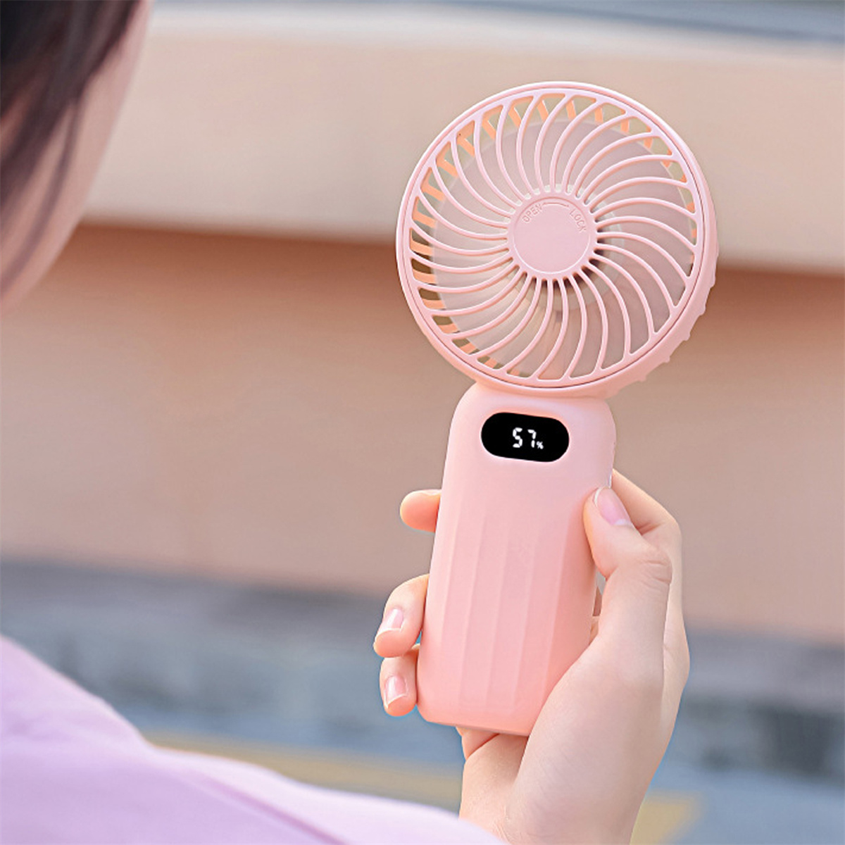 Eine Person hält einen rosa Mini-Ventilator mit digitaler Anzeige von 57 % Akku.