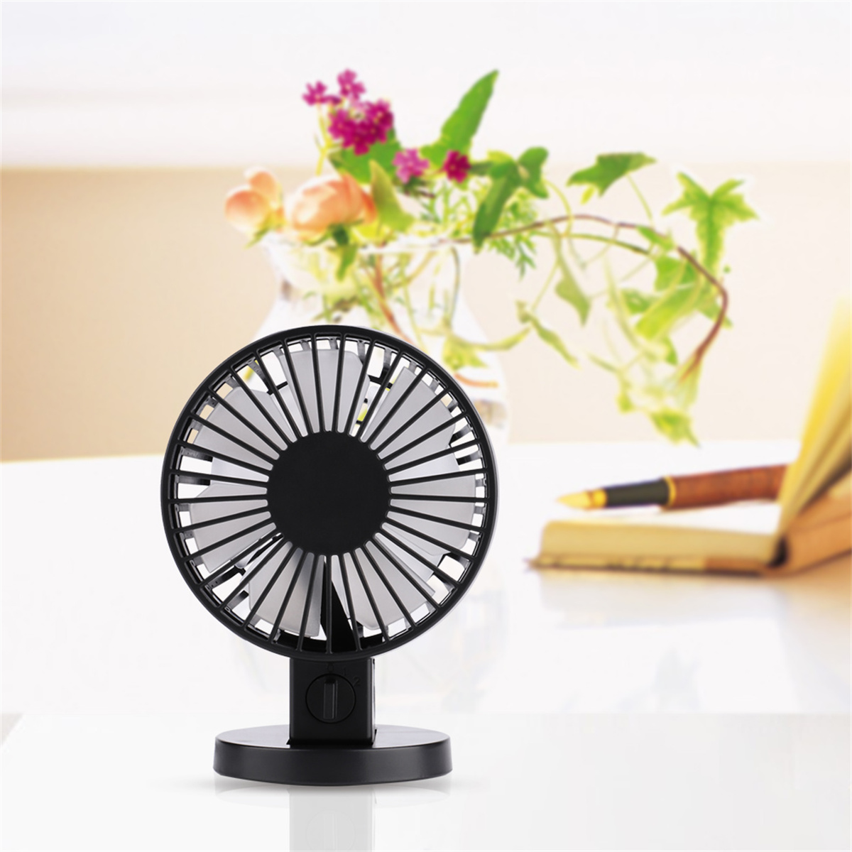 Ein schwarz-weißer Ventilator auf weißer Oberfläche mit einer Blumenvase und einem Buch, isoliert auf weißem Hintergrund.