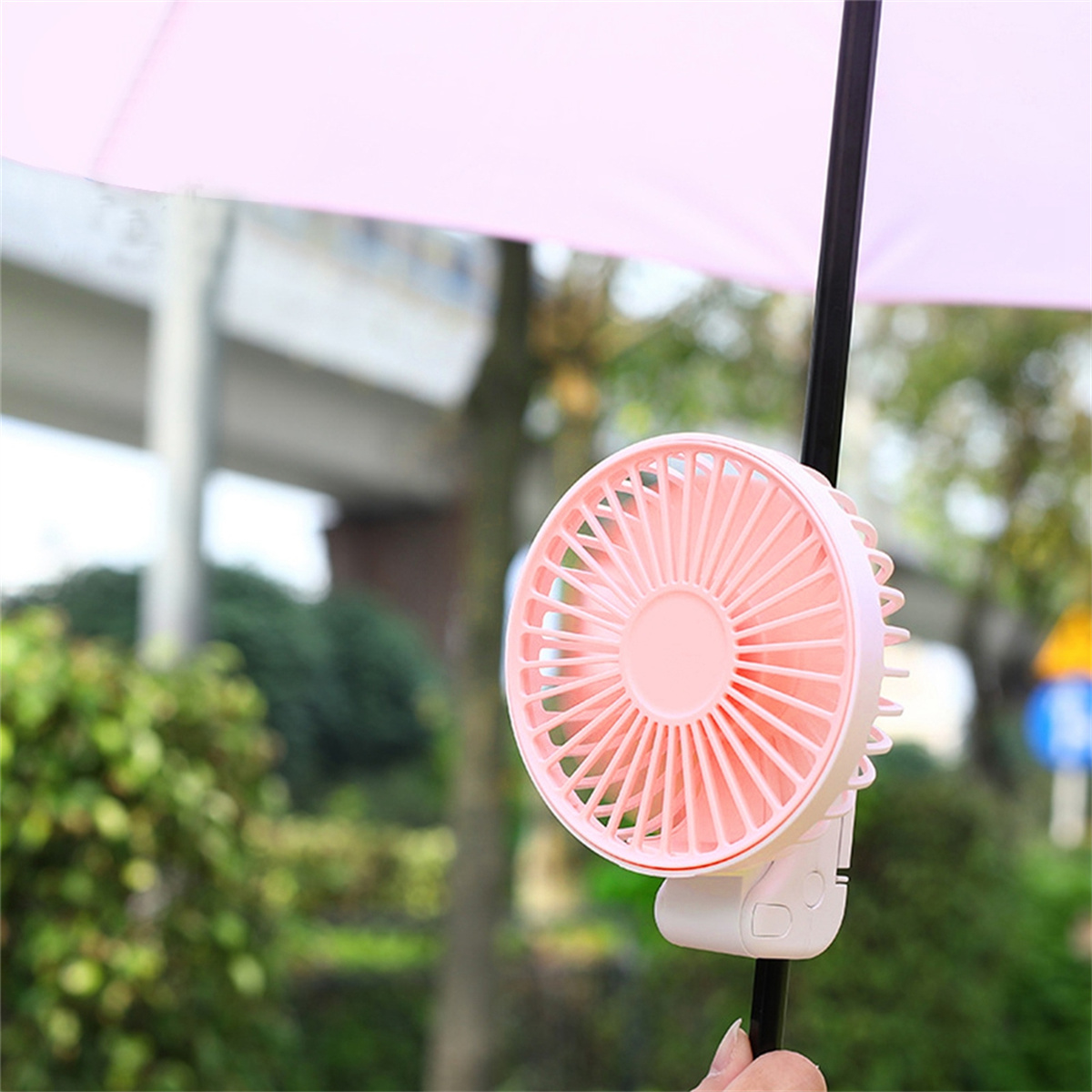 Ein rosa Ventilator an einem schwarzen Regenschirm befestigt. Der Ventilator ist rund.