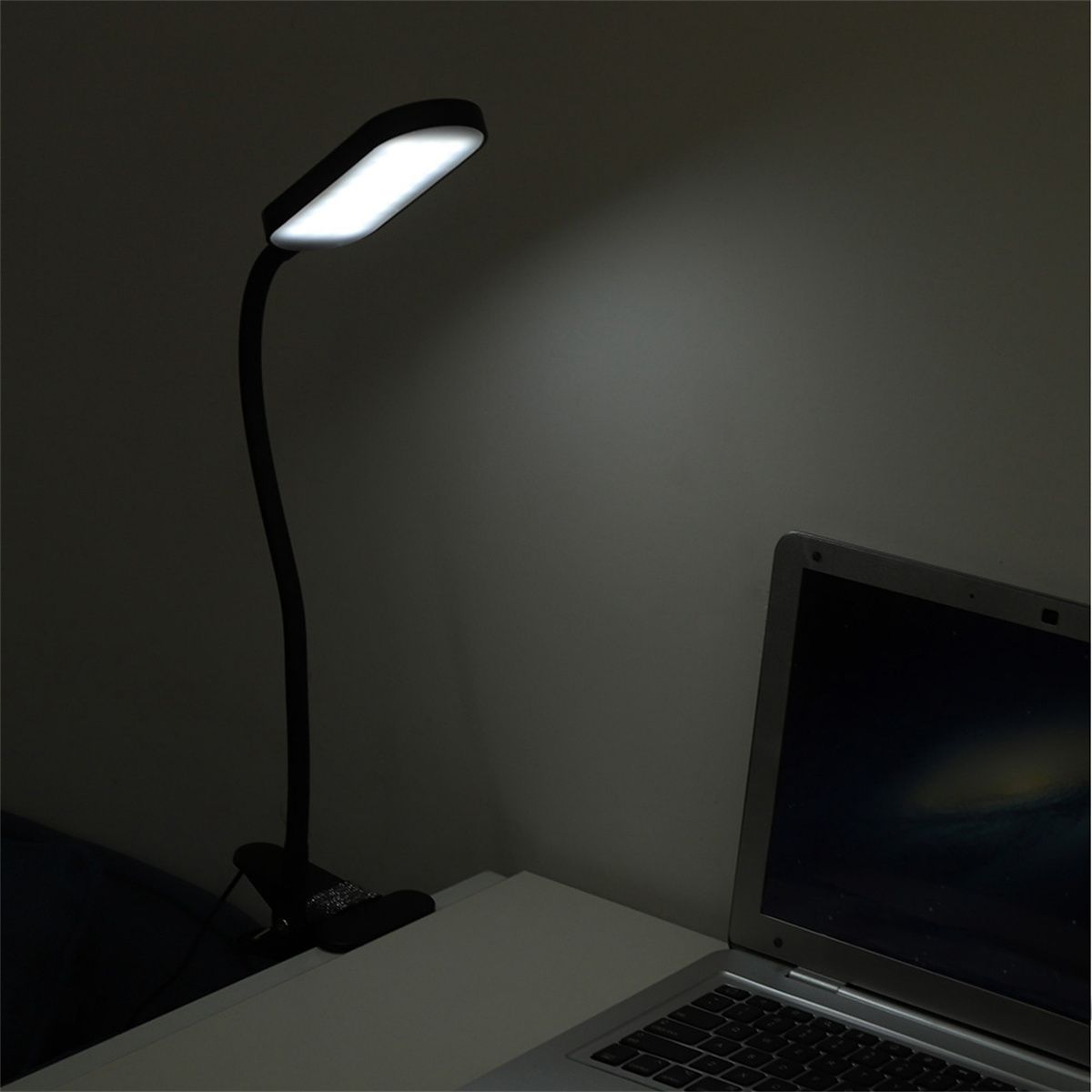 Schwarze Schreibtischlampe mit flexiblem Arm und rechteckigem Licht. Sie scheint Licht auf eine weiße Oberfläche und einen Laptop.