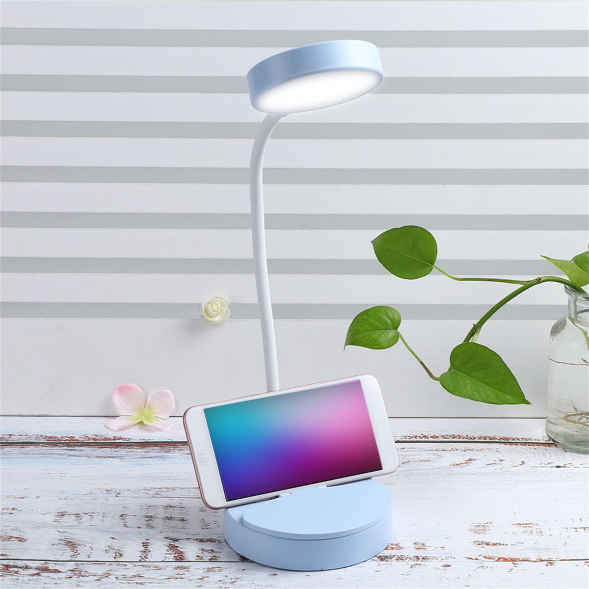 Eine blaue Schreibtischlampe mit einem Telefon auf dem Sockel, das einen farbenfrohen Bildschirm zeigt.