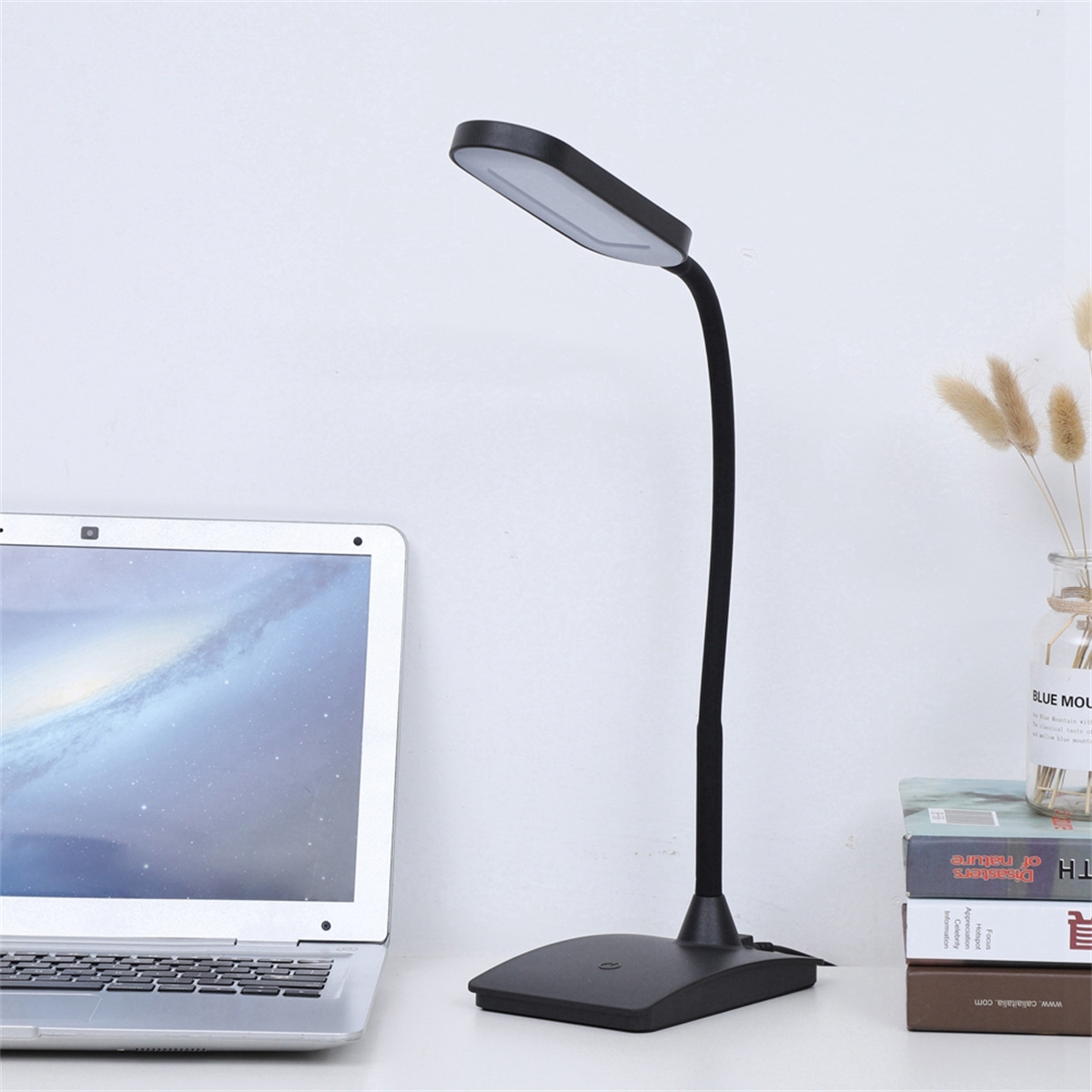 Schwarze Schreibtischlampe mit gebogenem Arm und rechteckigem Licht, auf einem Schreibtisch.