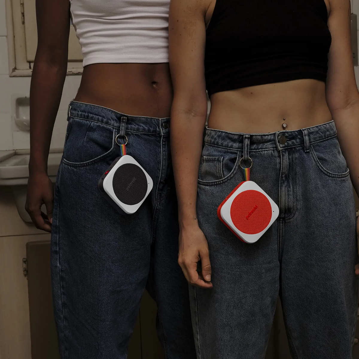 Dwie osoby w dżinsach trzymają głośniki wiszące na szlufkach od paska.