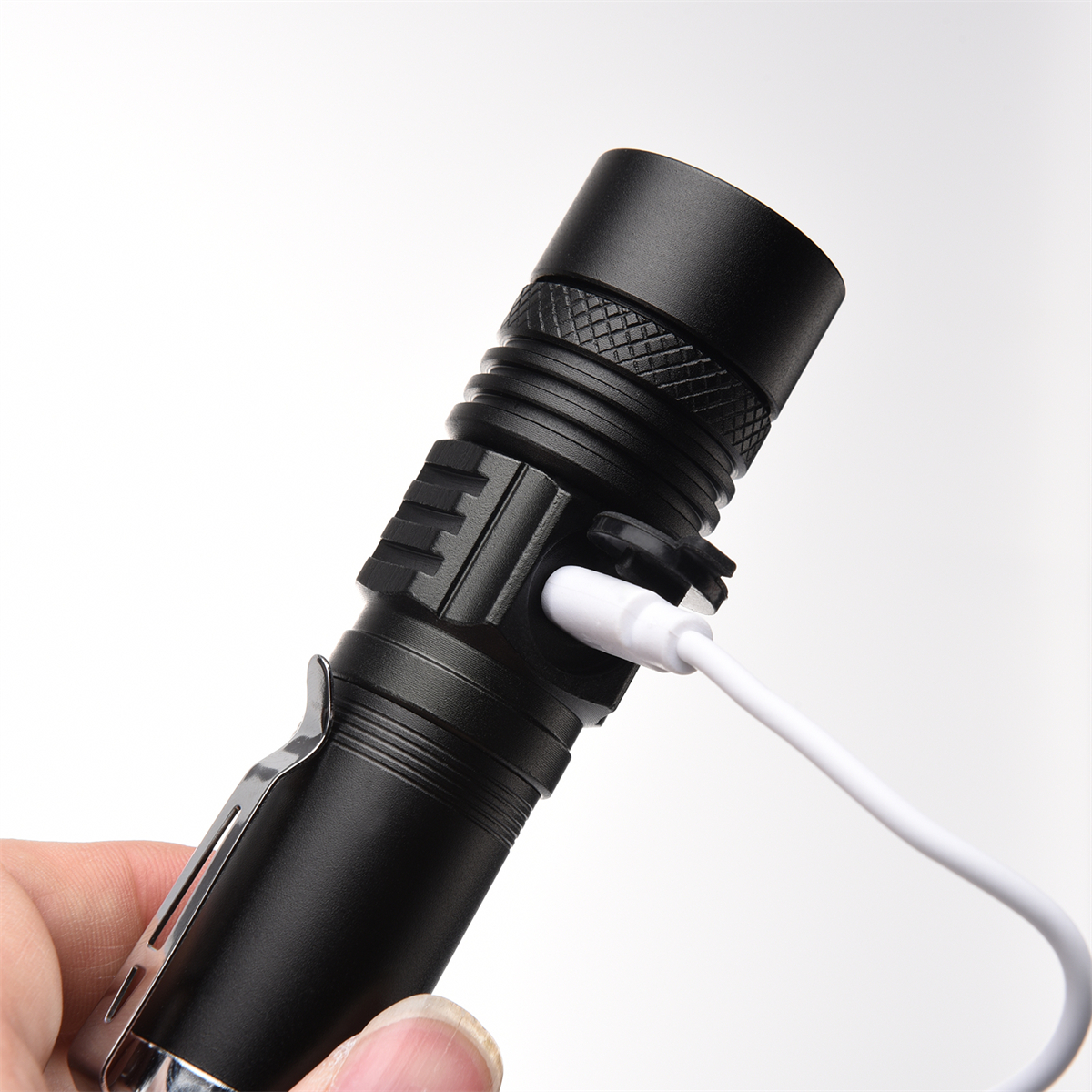 Schwarze Taschenlampe mit eingestecktem USB-Ladekabel, gehalten von einer Hand, weißer Hintergrund.