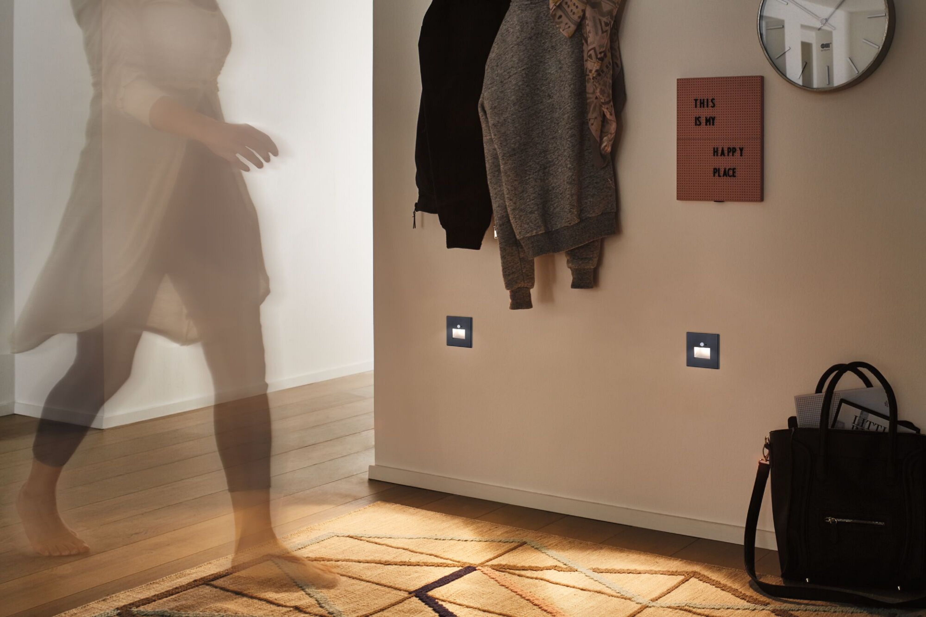 Eine Person geht in einem Flur mit Lichtern an der Wand und einem Teppich. Das Innere ist modern.