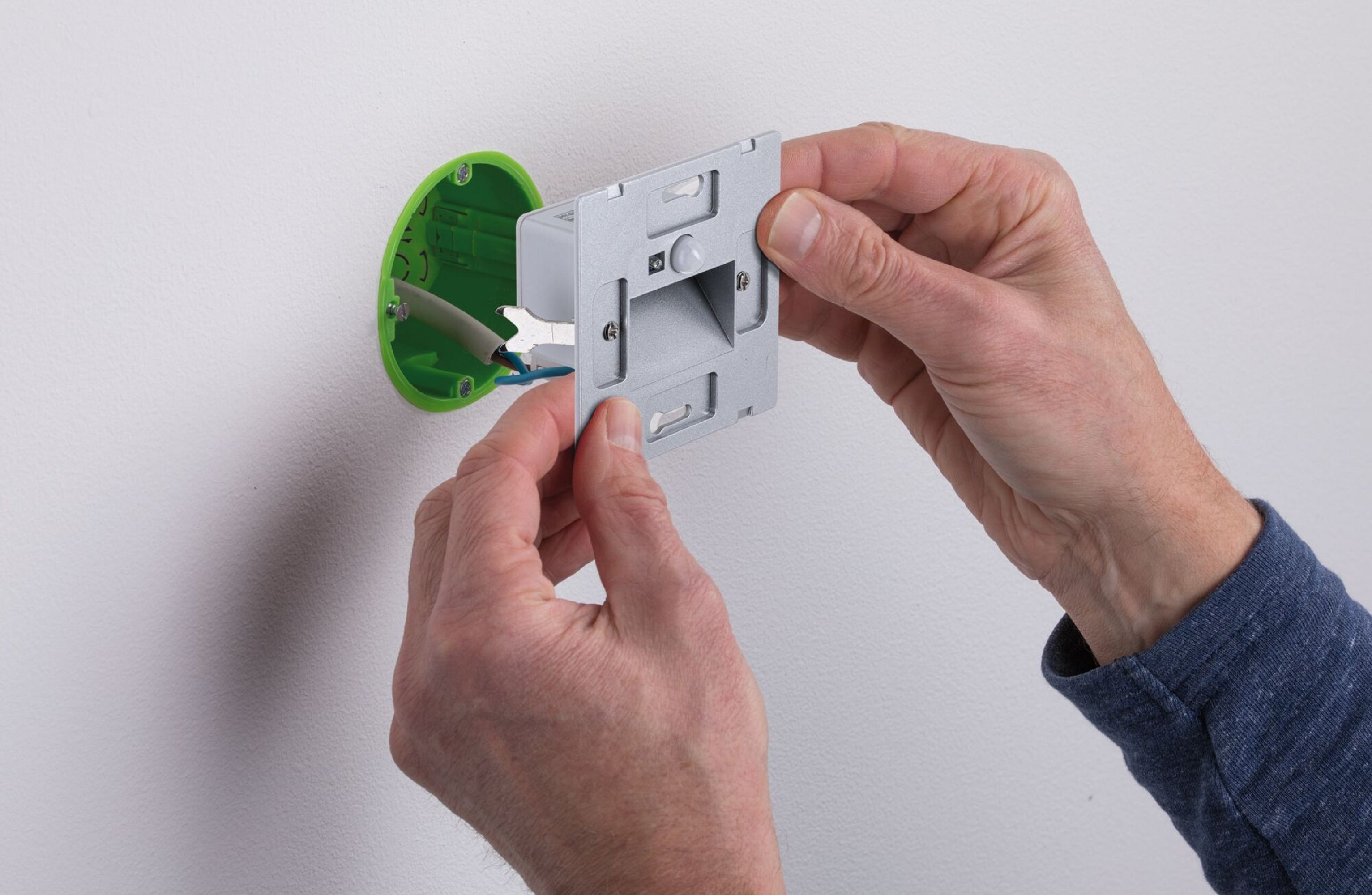 Mani che installano un interruttore bianco in una scatola verde su una parete bianca.