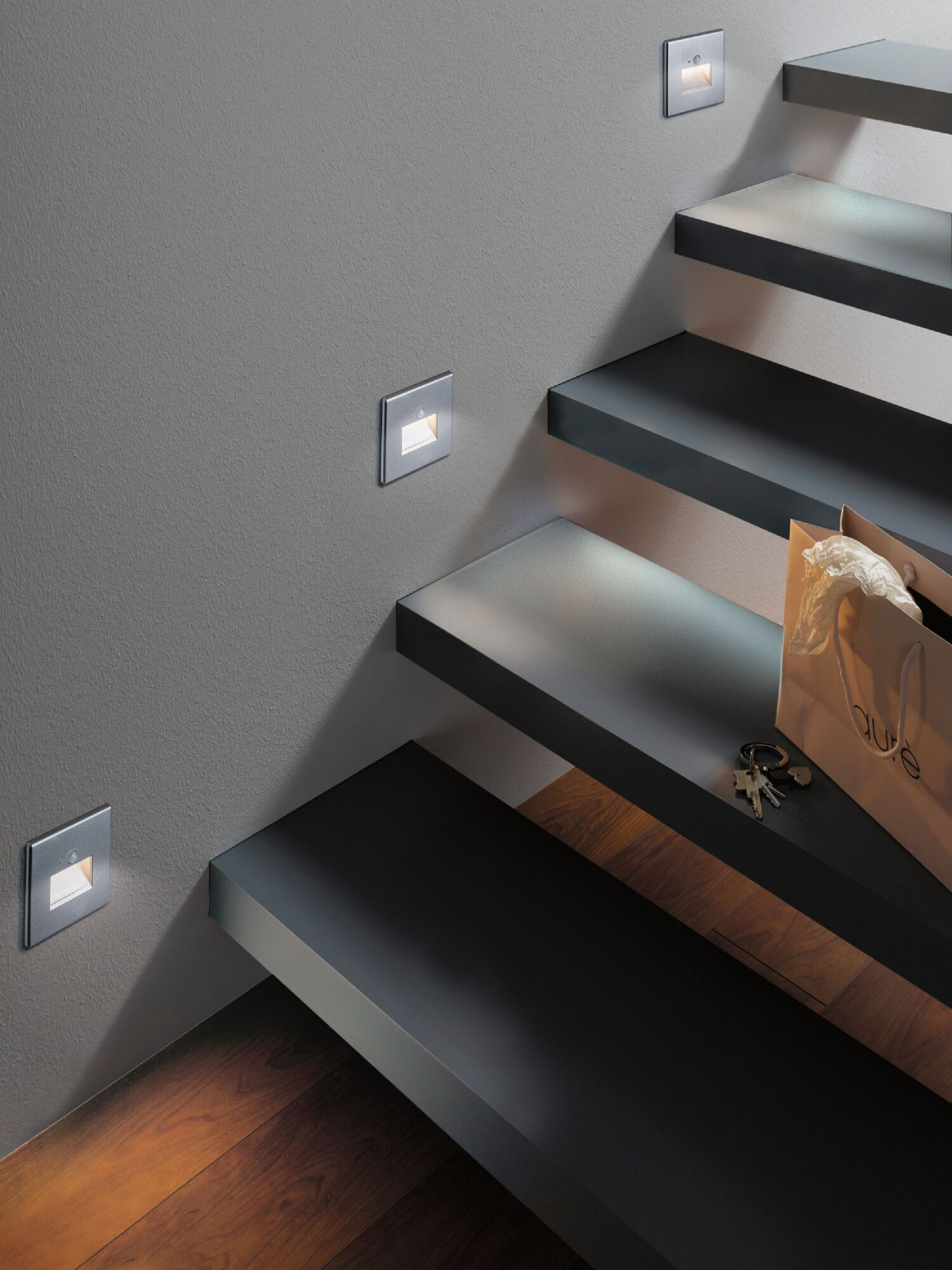 Treppe mit Einbauleuchten an Wand und Stufen. Tasche und Schlüssel liegen auf einer Stufe.