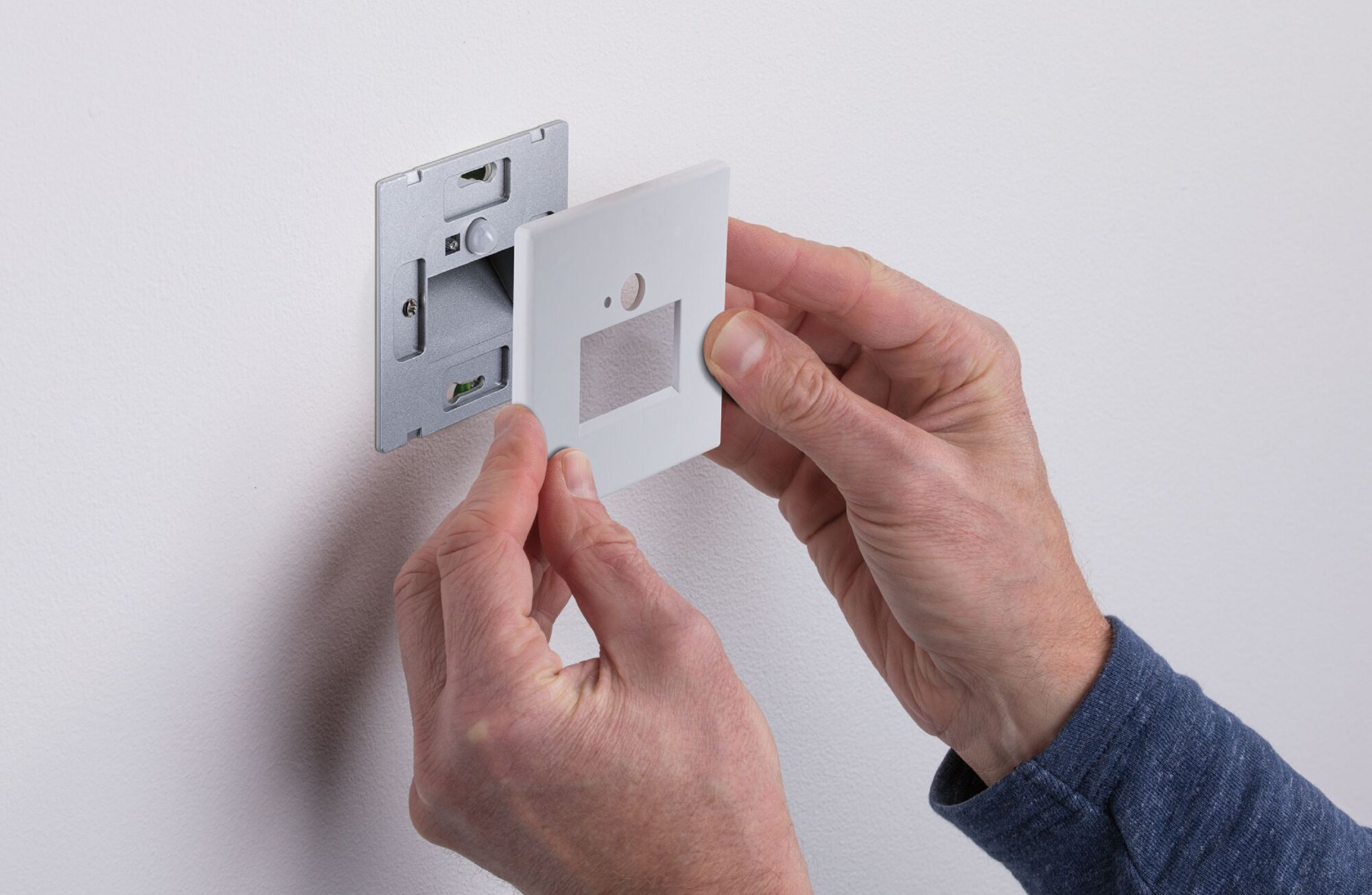 Die Hände einer Person installieren einen weißen Lichtschalter an einer Wand mit einem Metallrahmen.