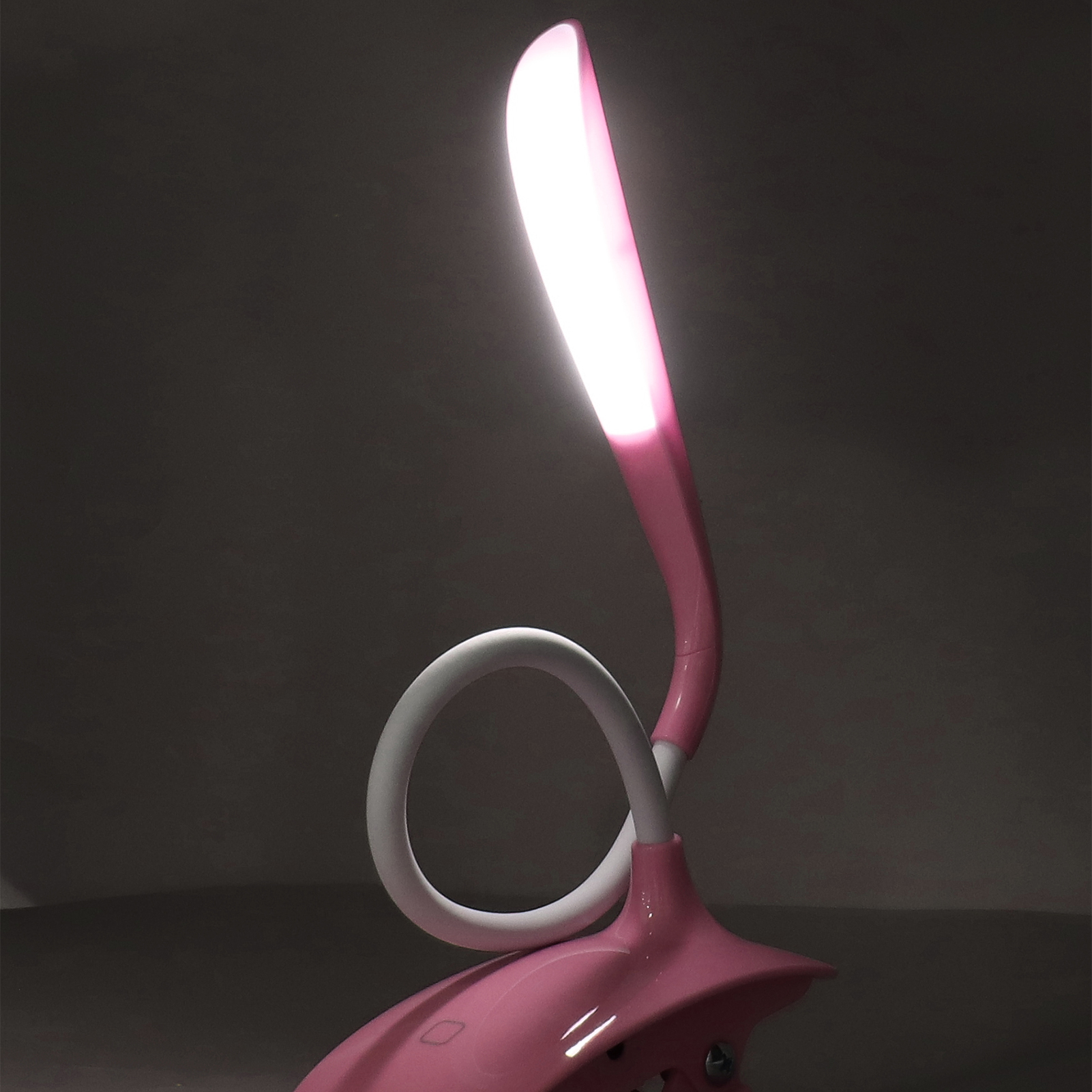 Pinkfarbene Schreibtischlampe mit weißem, flexiblem Hals, leuchtet rosa. Dunkler Hintergrund.