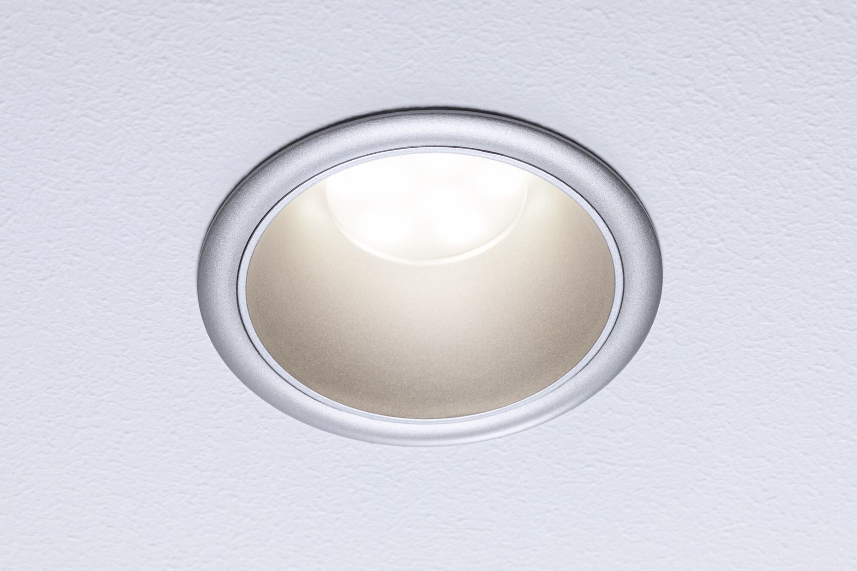 Wpuszczana lampa sufitowa. Srebrna ramka. Jasne światło emanujące ze środka.