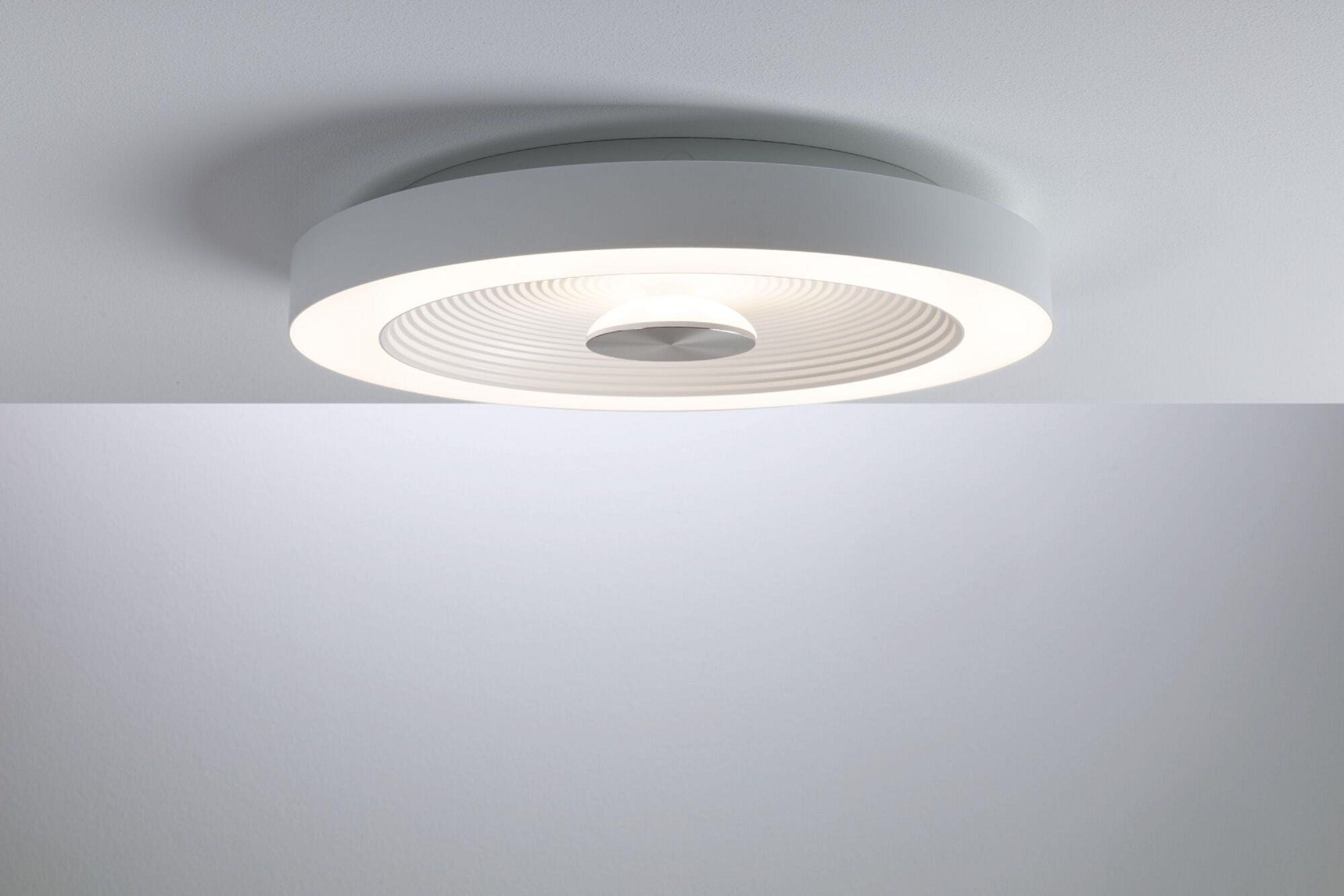 Weiße Deckenlampe mit rundem Design und Lichtquelle in der Mitte. Sie wirft einen Schatten.