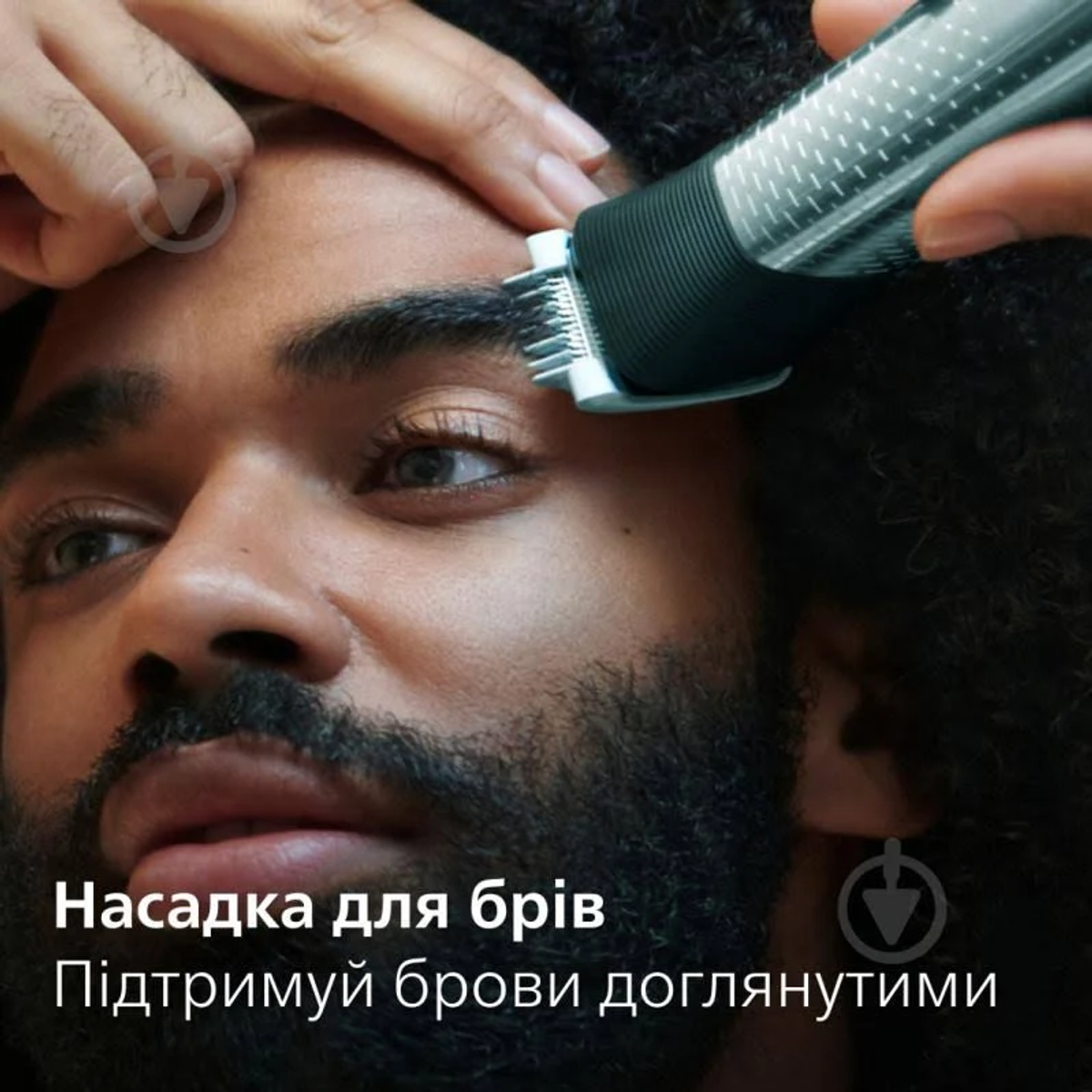 Un hombre recorta sus cejas con una recortadora eléctrica. Texto en ucraniano en la imagen.