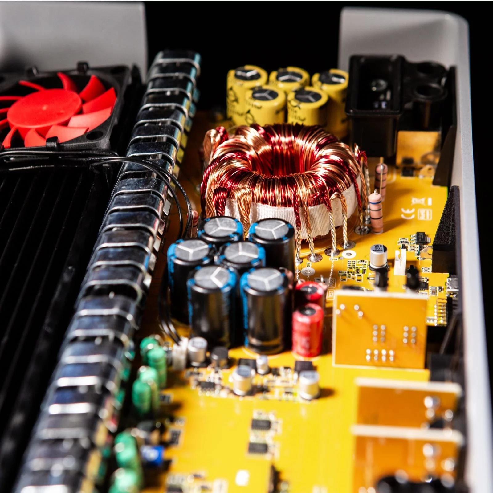 Geöffnete Elektronik mit rotem Lüfter, Drähten und gelben Komponenten. Der Hintergrund ist schwarz.