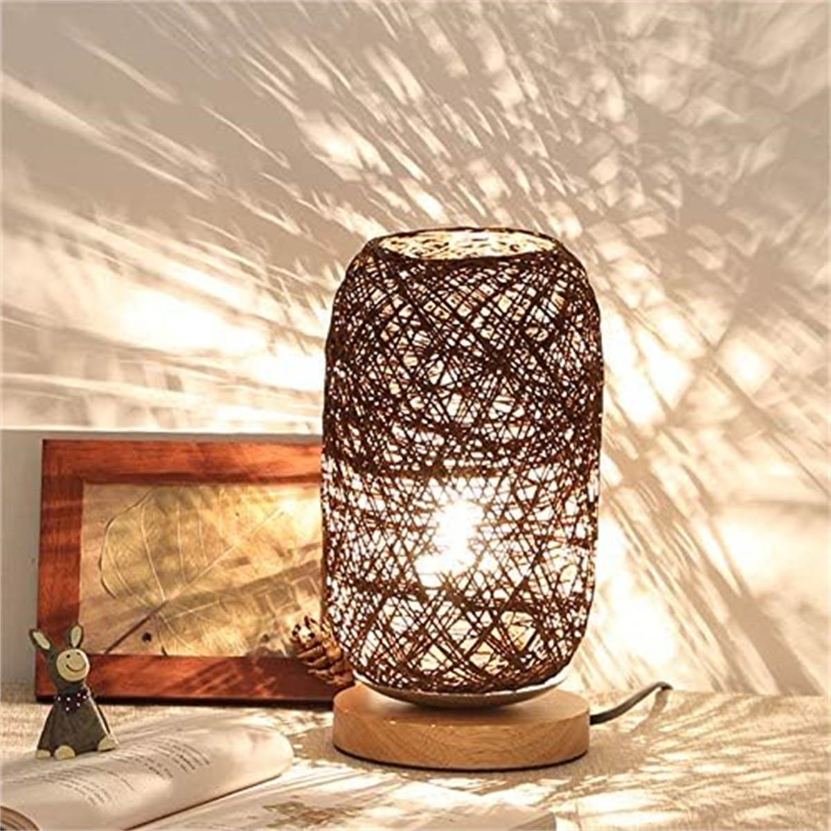 Tischlampe mit gewebtem braunen Schirm, Holzsockel und einem Buch.