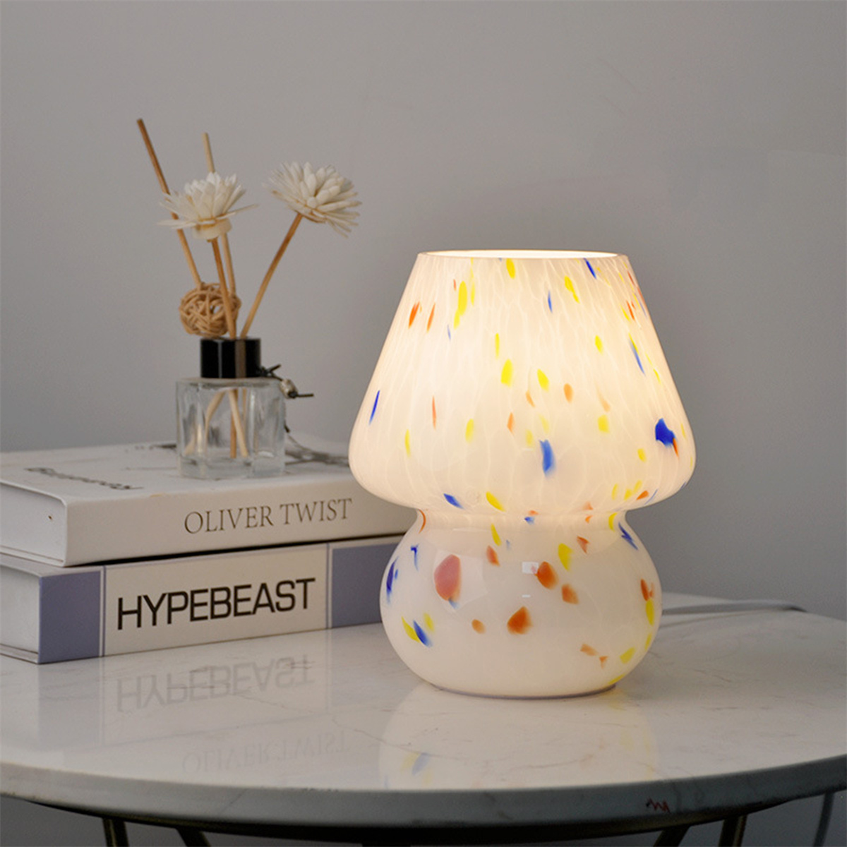 Pilzförmige Lampe mit bunten Punkten. Sie steht auf einem Tisch mit Büchern und Deko.