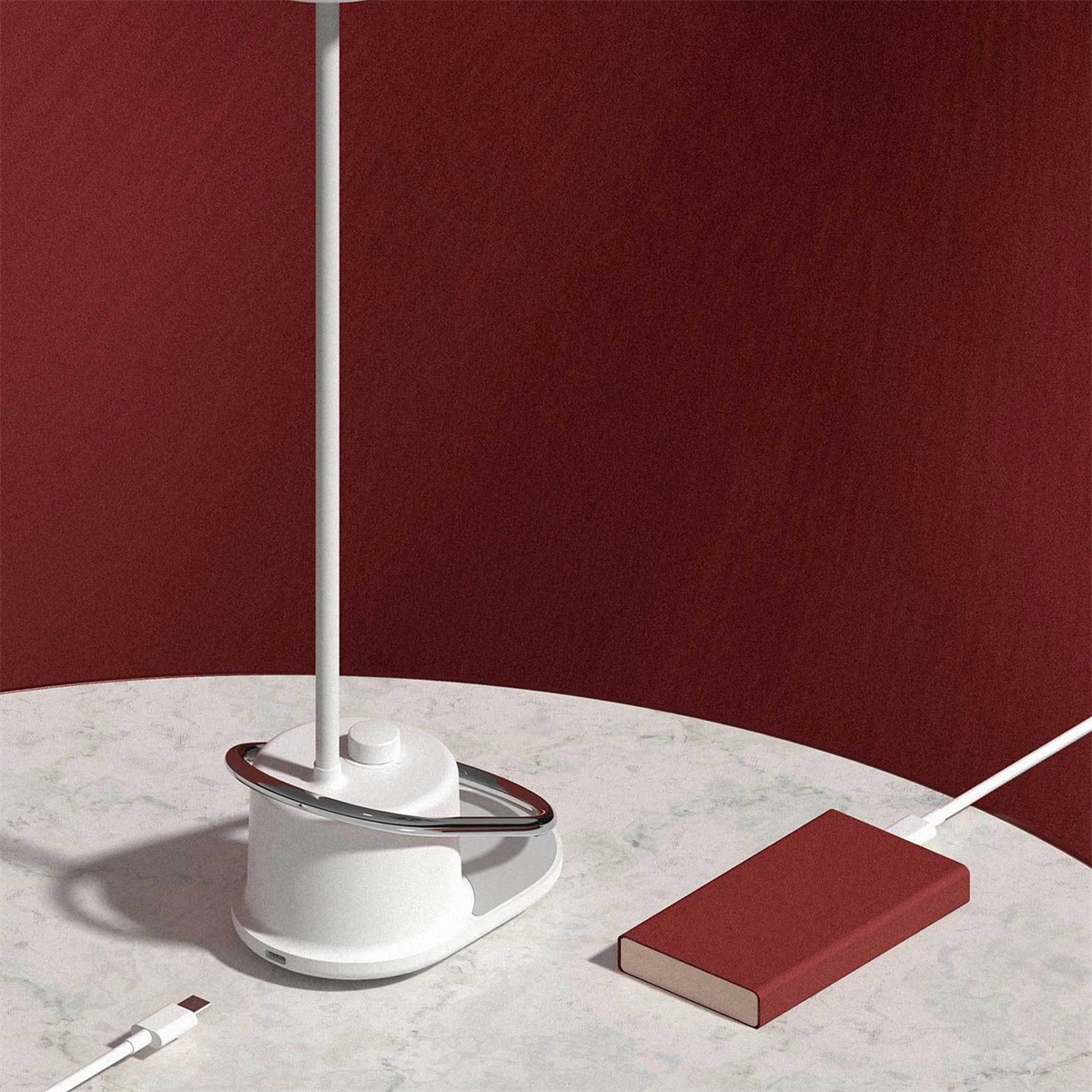 Eine weiße Lampe mit silbernem Ring auf einem Tisch. Eine rote Powerbank und ein weißes Kabel daneben.