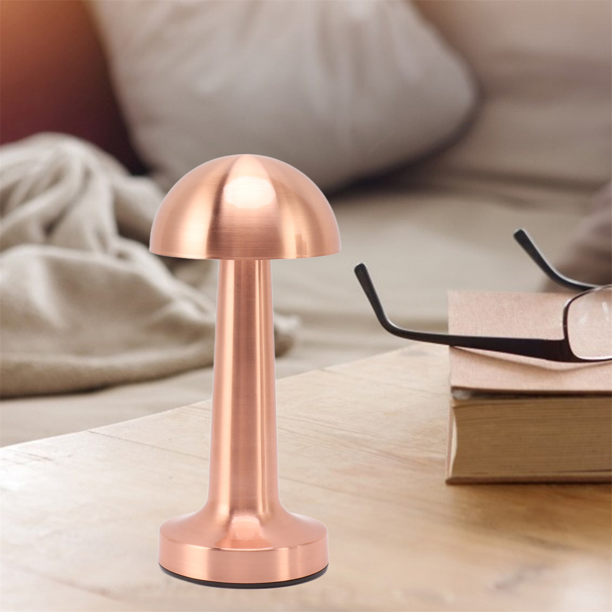 Kupferfarbene pilzförmige Lampe auf einem Holztisch mit Brille und Büchern.