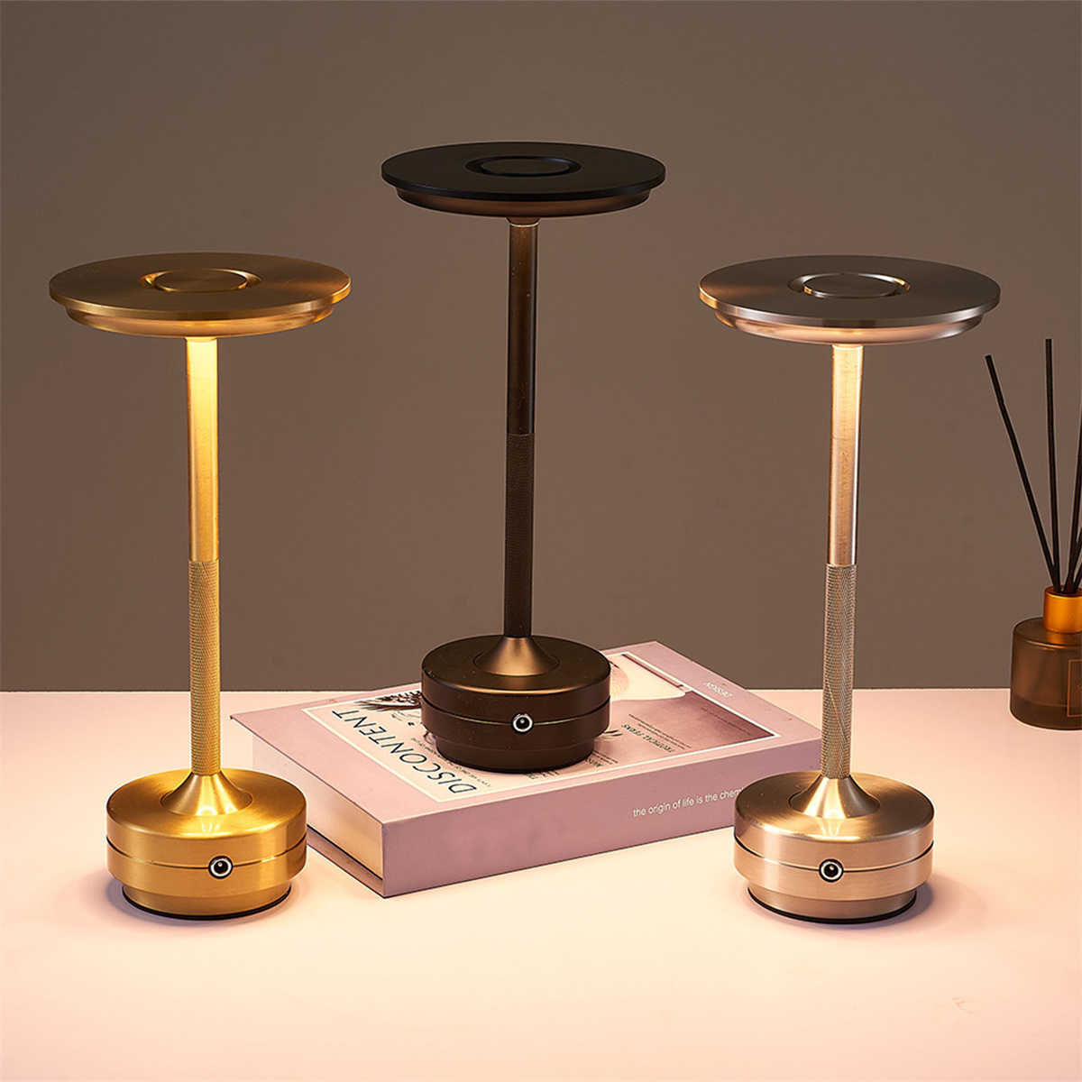 Drei elegante Tischlampen mit Gold- und Bronzefinish, leuchtend. Buch und Diffusor daneben.